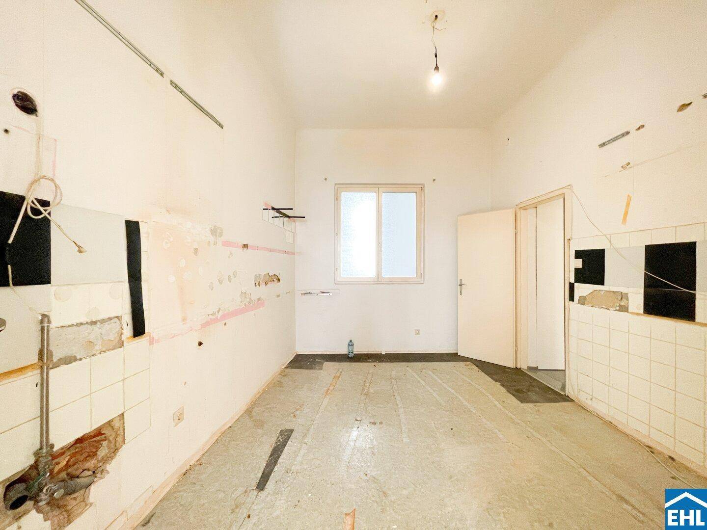 Renovierungsbedürftige Küche mit Fliesen an den Wänden und einem Fenster, bereit für eine Neugestaltung.