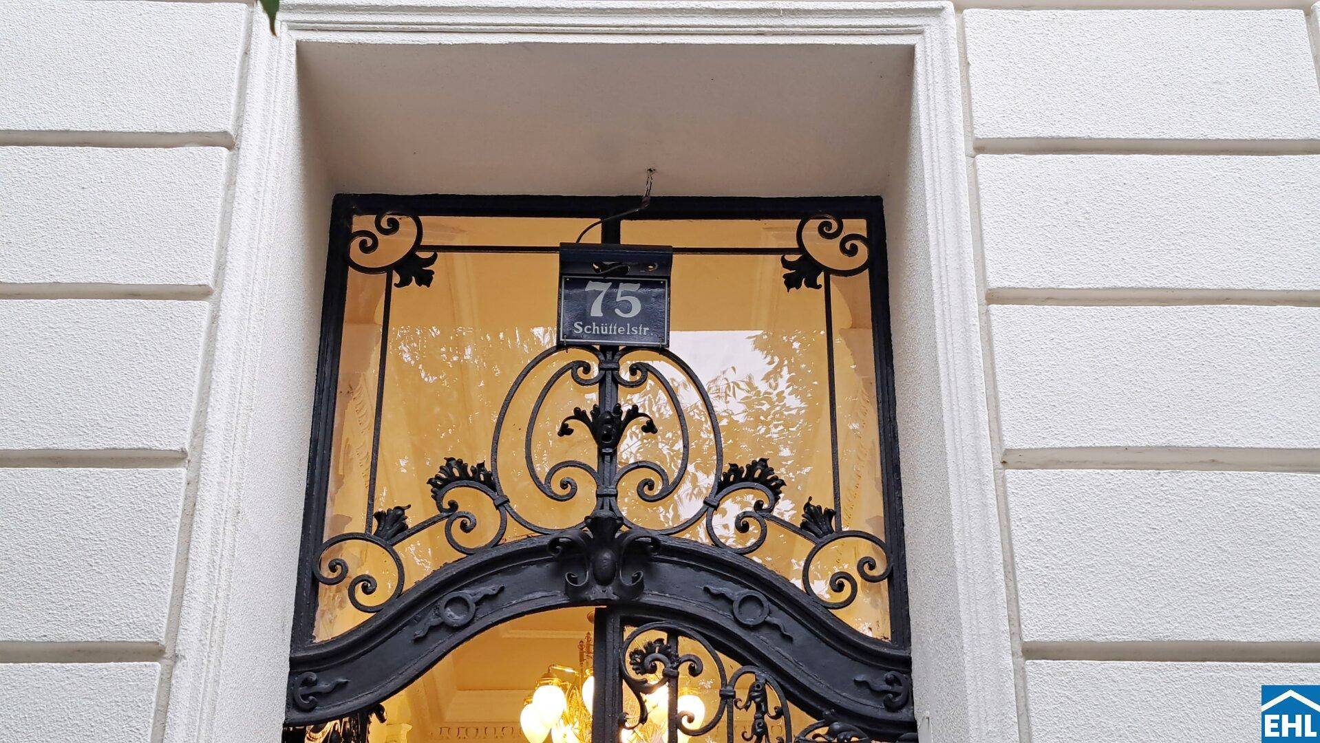 Eingangsbereich mit schmiedeeisernem Tor und Hausnummer 75 an einer historischen Fassade.