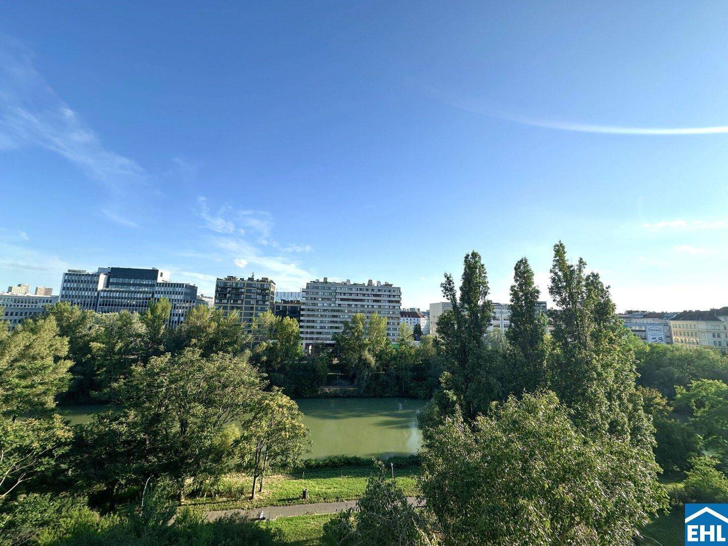 Weitläufiger Blick vom Balkon über eine grüne Parkanlage mit Wasser und städtischen Gebäuden.
