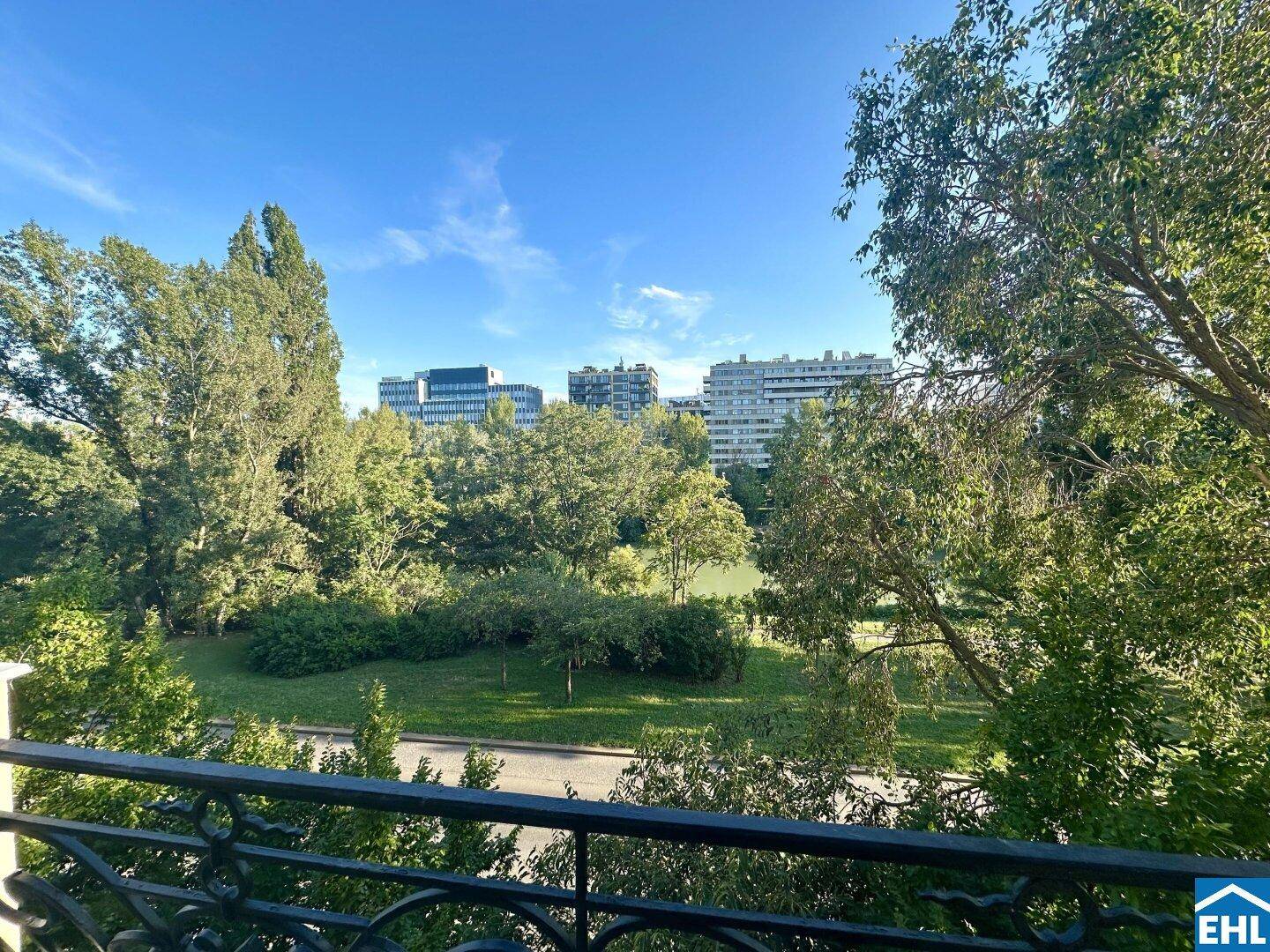 Blick vom Balkon auf eine grüne Parklandschaft mit See und städtischer Skyline im Hintergrund.