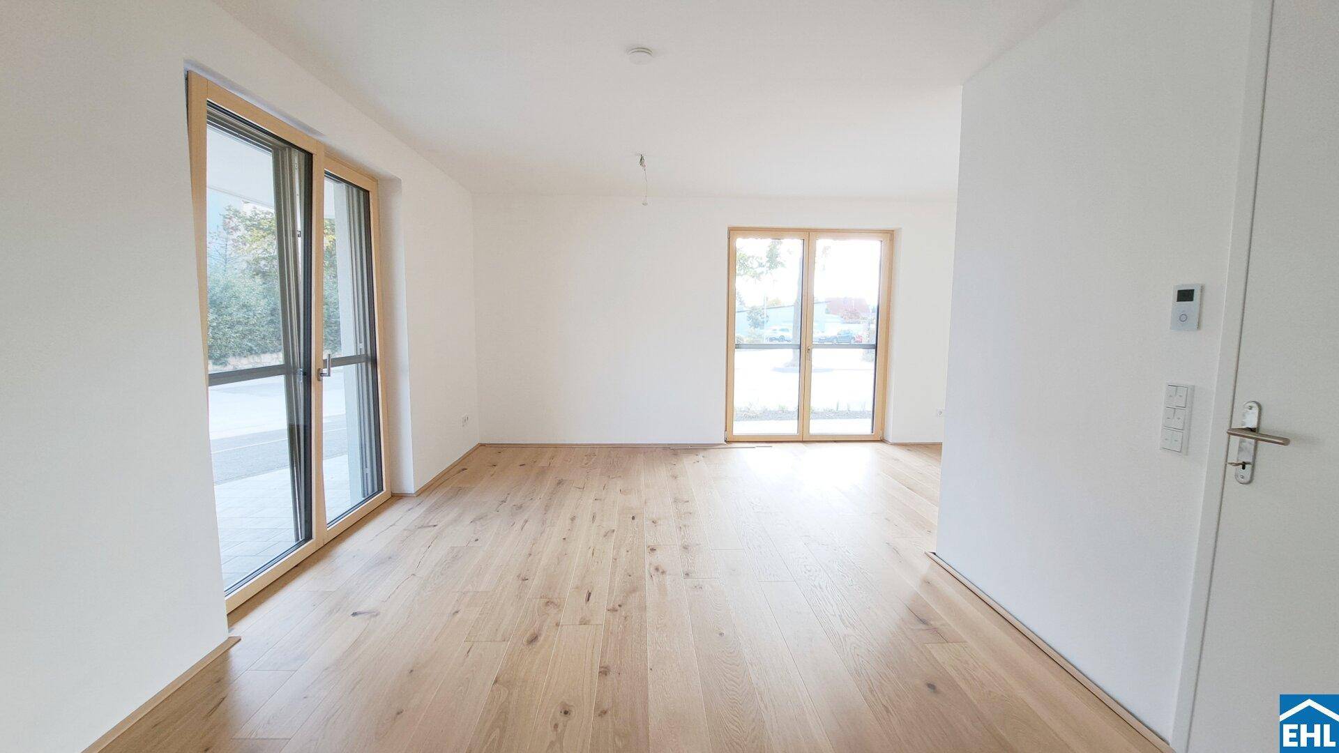Geräumiger, heller Raum mit Parkettboden und mehreren Fenstertüren, die ins Freie führen.