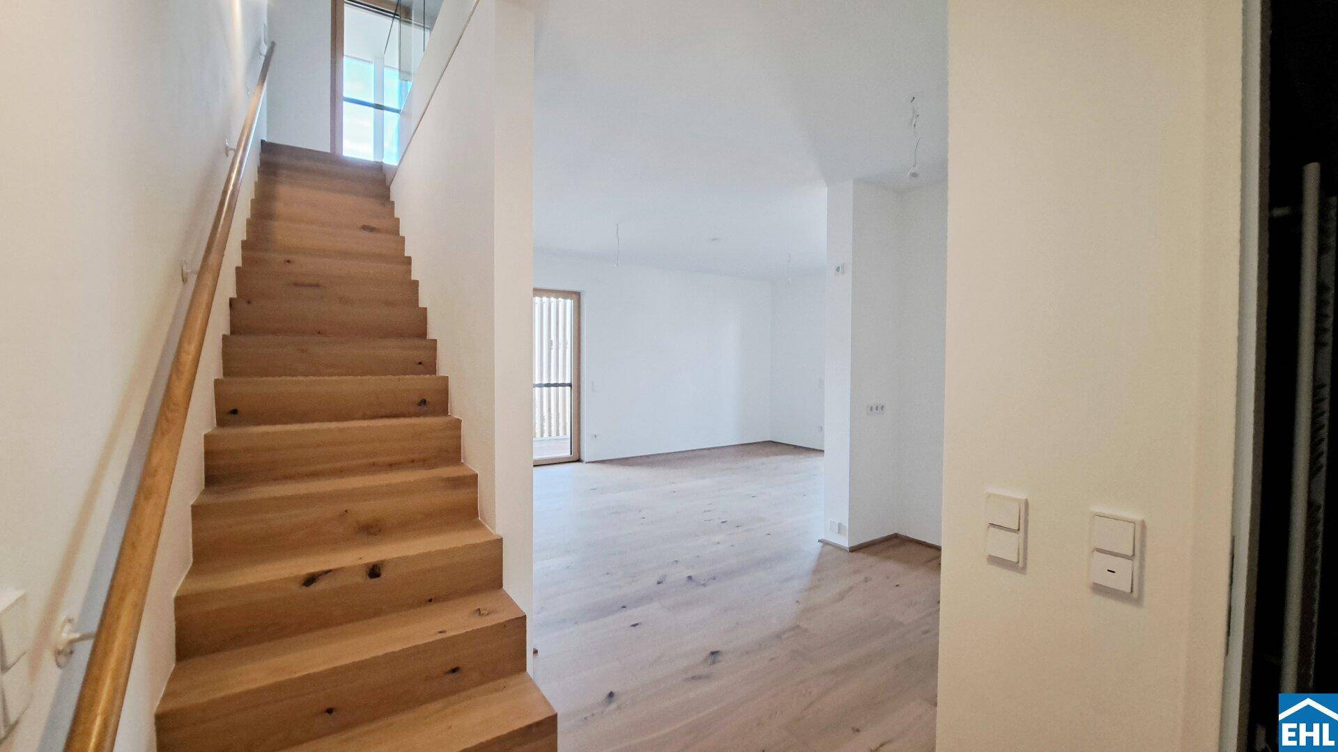 Helle Holztreppe führt in das obere Stockwerk, mit Blick auf einen Wohnbereich.