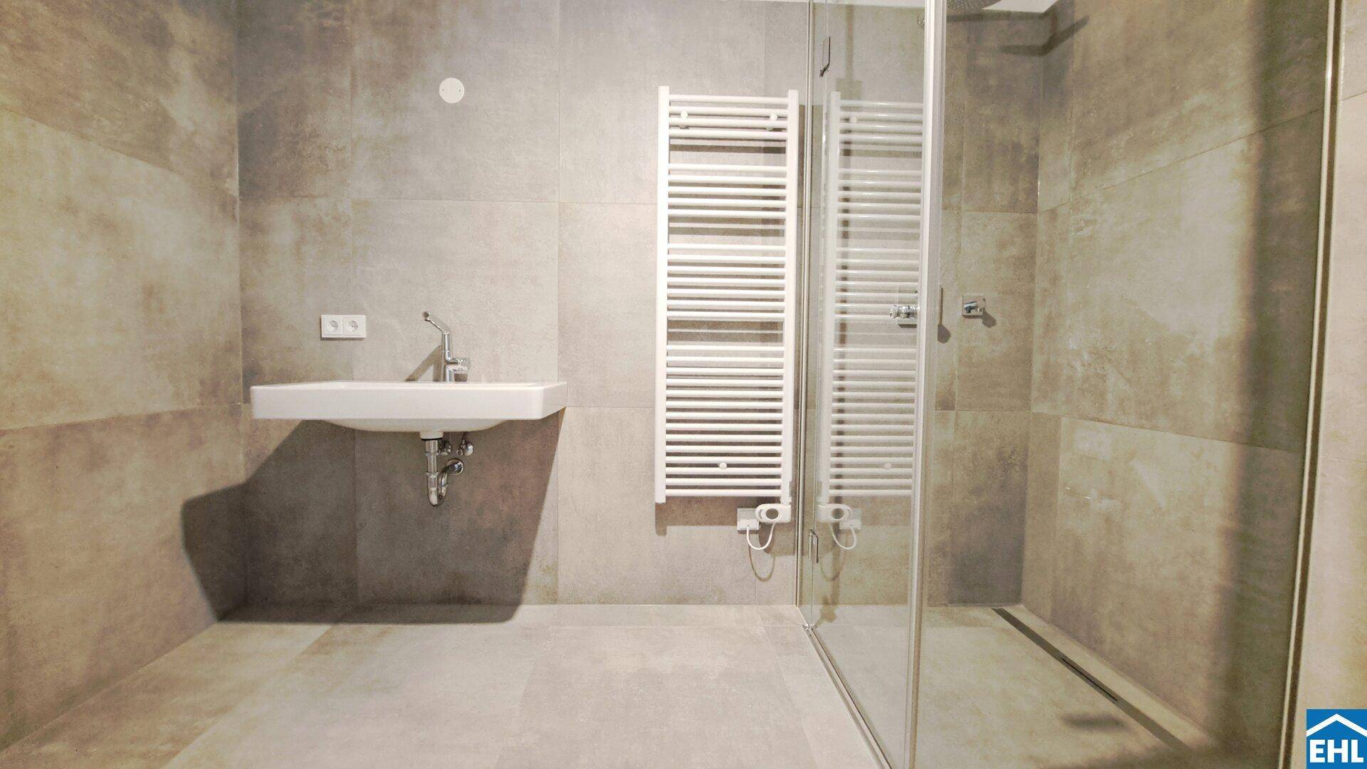 Modernes Badezimmer mit grauen Fliesen, wandhängendem Waschbecken und begehbarer Dusche.