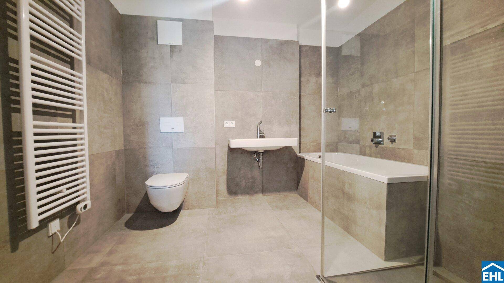 Modernes Badezimmer mit grauen Fliesen, Badewanne und separater Dusche.