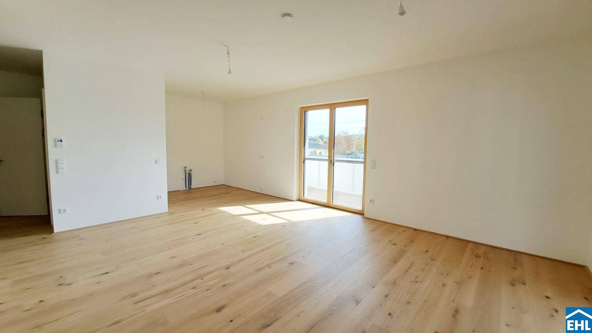 Geräumiger, lichtdurchfluteter Wohnbereich mit hellem Parkettboden und großem Fenster mit Balkonzugang.