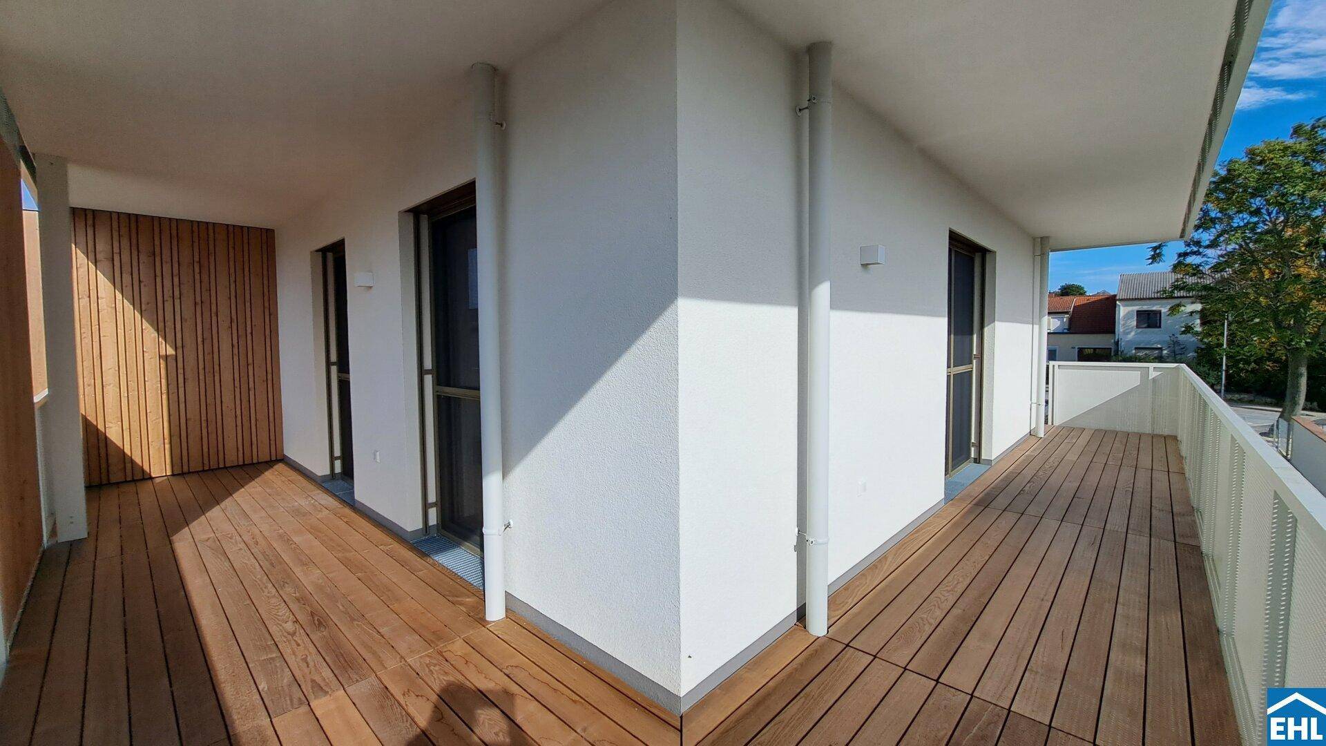 Geräumiger Eckbalkon mit Holzfußboden und moderner weißer Brüstung, ideal für Entspannung im Freien.