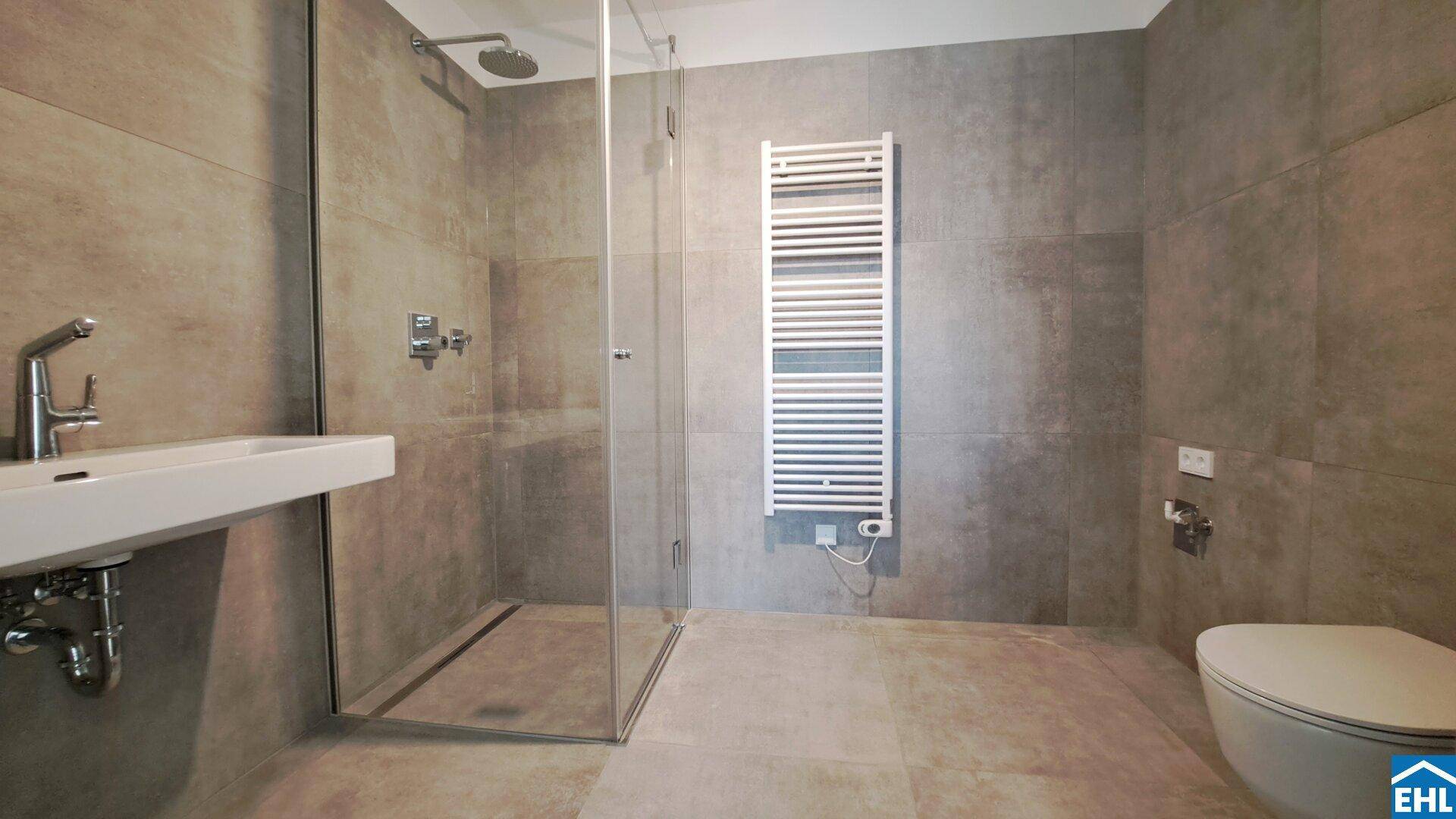 Modernes Badezimmer mit grauen Fliesen, ebenerdiger Dusche, Einzelwaschbecken und Handtuchheizkörper.