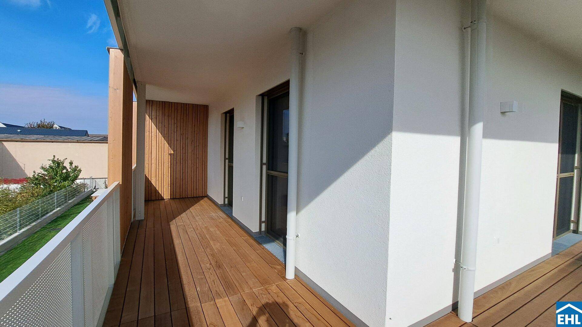 Langer Balkon mit Holzboden und weißer Brüstung, ergänzt durch eine stilvolle Holzwandverkleidung.