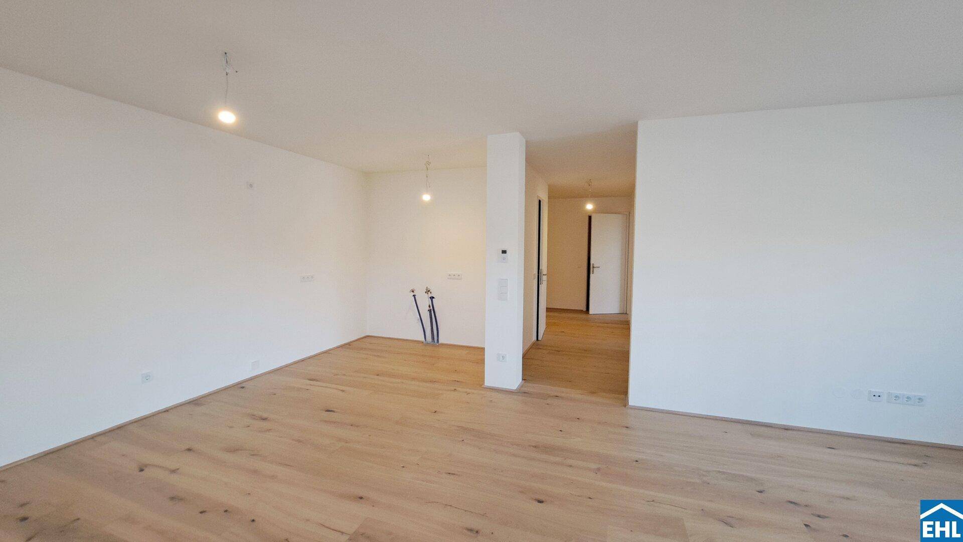Offener Raum mit Holzboden und vorbereiteten Anschlüssen für eine Küche.