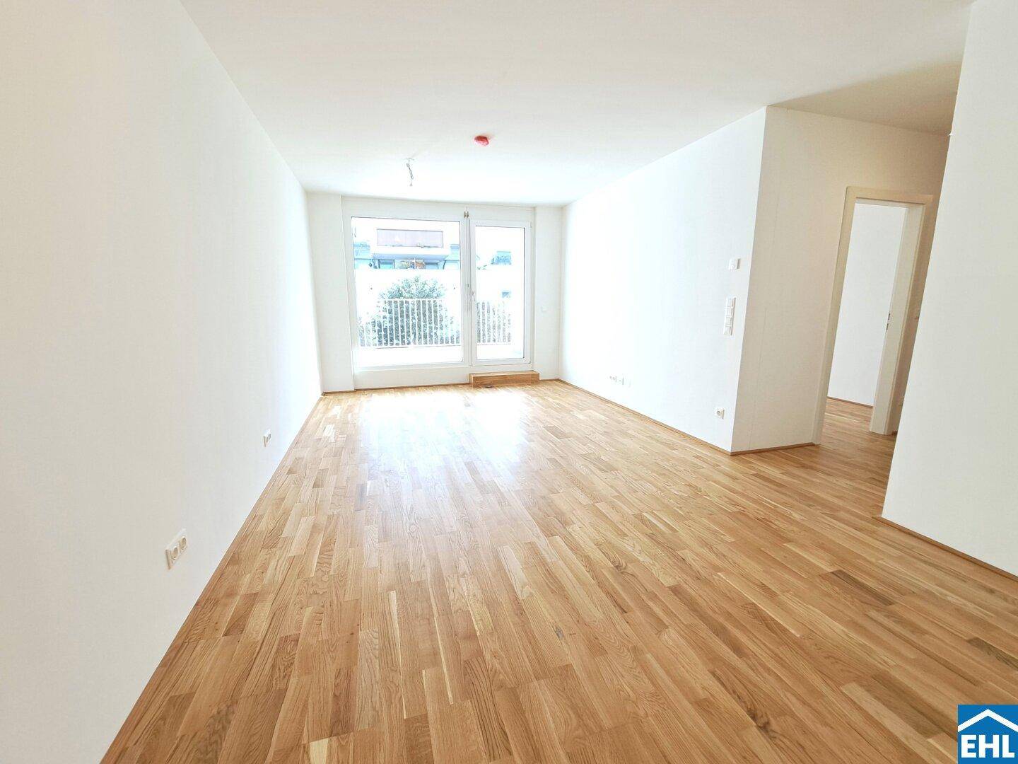 Helles, leeres Wohnzimmer mit Holzboden und Zugang zu einem französischen Balkon.