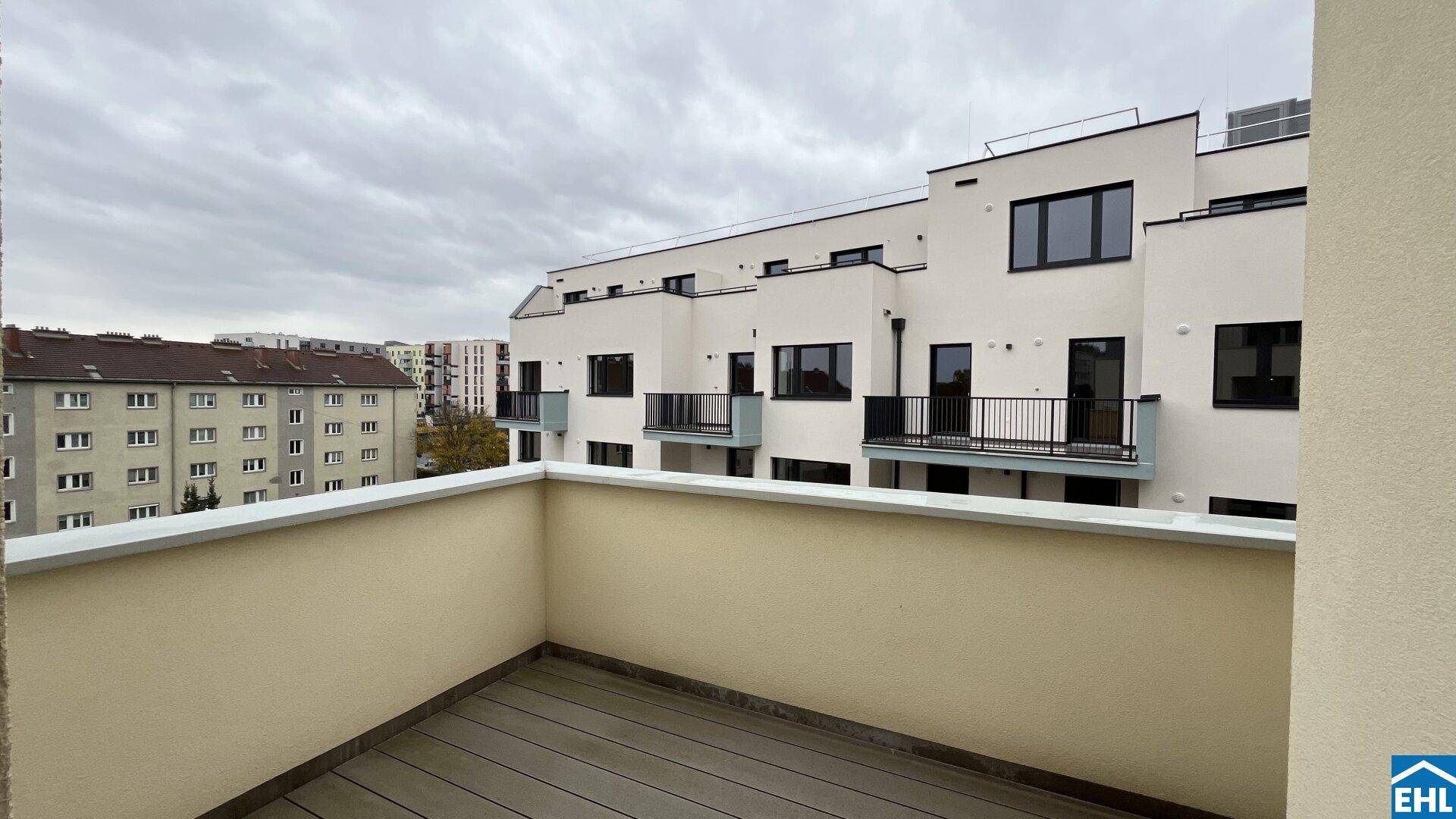 Leerer Balkon mit Holzboden und Blick auf die moderne Architektur der Wohnanlage.