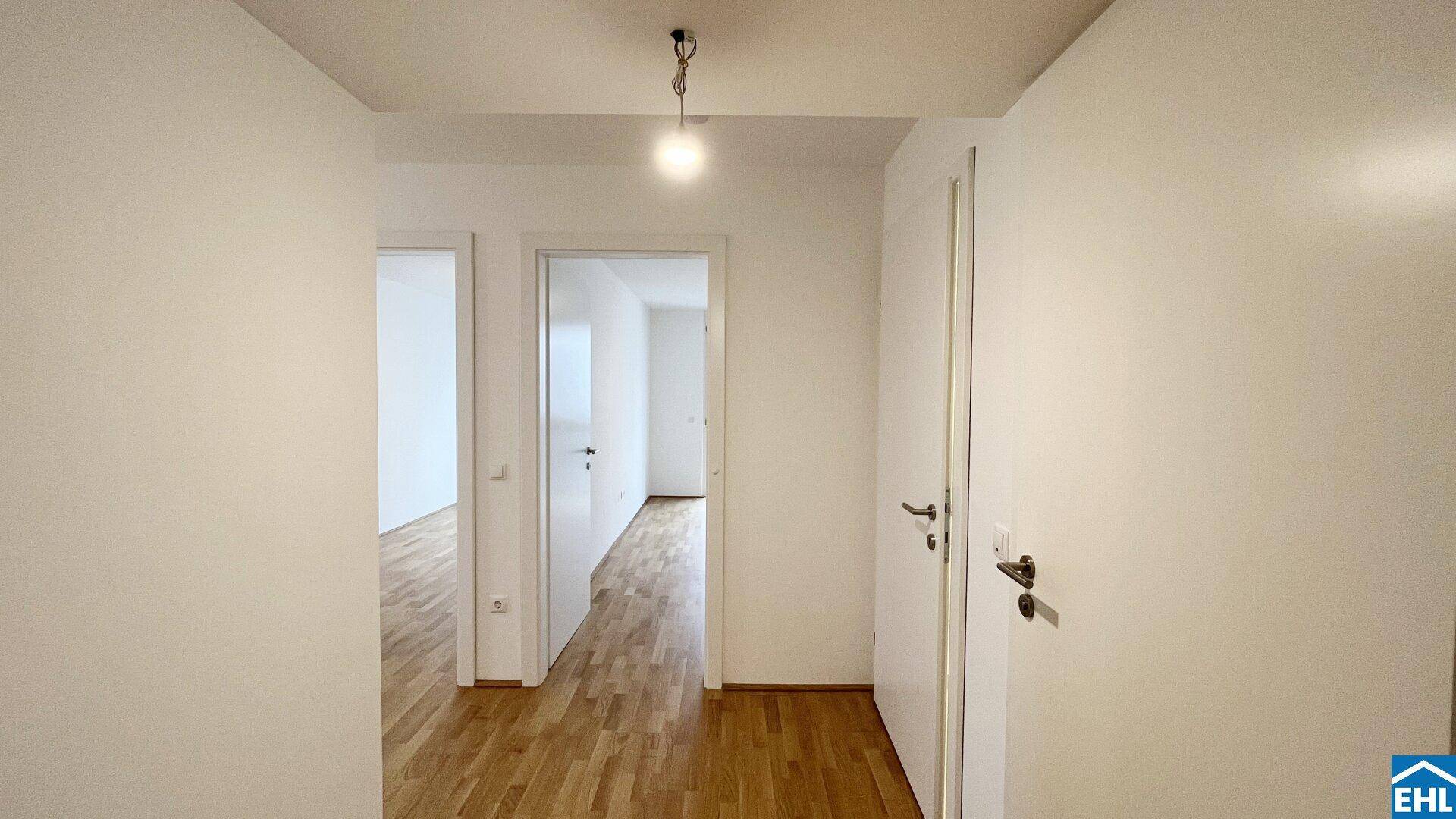 Heller Flur mit Holzboden und weißen Wänden, der zu den verschiedenen Zimmern führt.