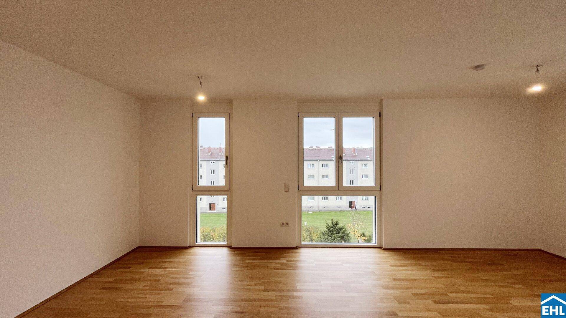 Geräumiger Wohnbereich mit Parkettboden und weitem Blick ins Grüne durch die großen Fenster.