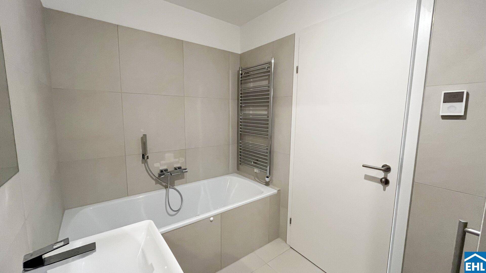 Modernes Badezimmer mit Badewanne, beheiztem Handtuchhalter und hellen, großformatigen Fliesen.