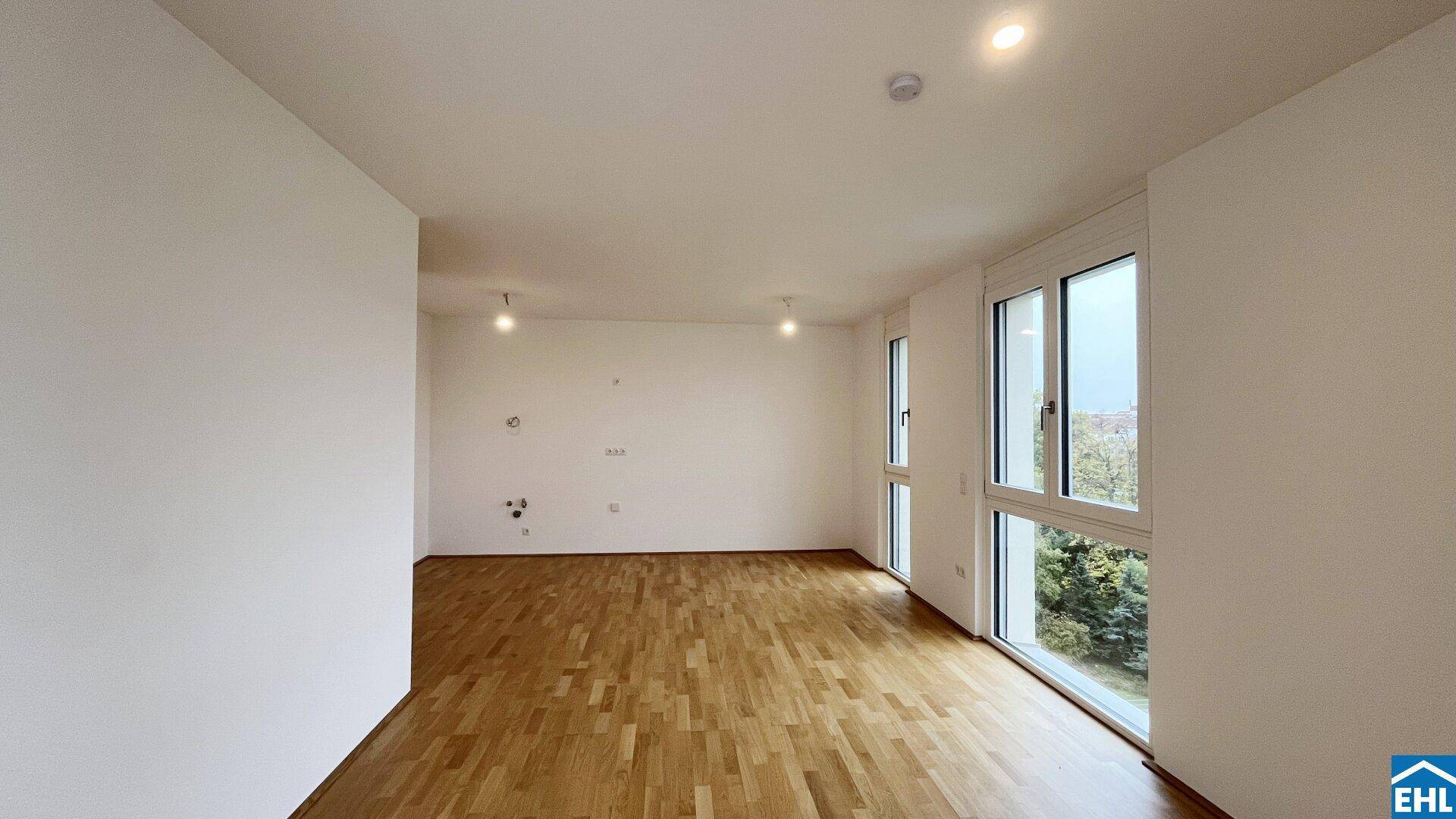 Heller, unmöblierter Wohnraum mit Holzboden und großen Fenstern, die einen schönen Grünblick bieten.