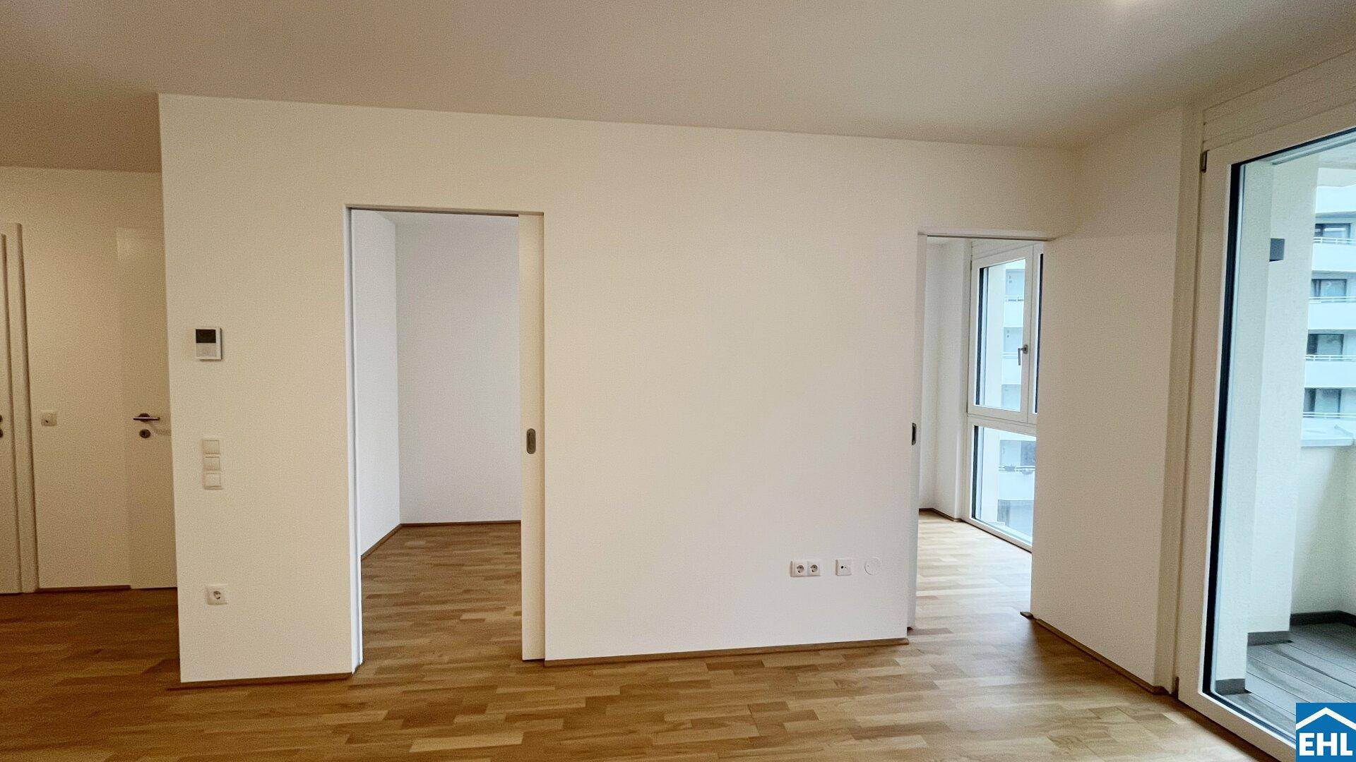 Heller Raum mit Holzboden, weißen Wänden und mehreren Türöffnungen zu angrenzenden Bereichen.