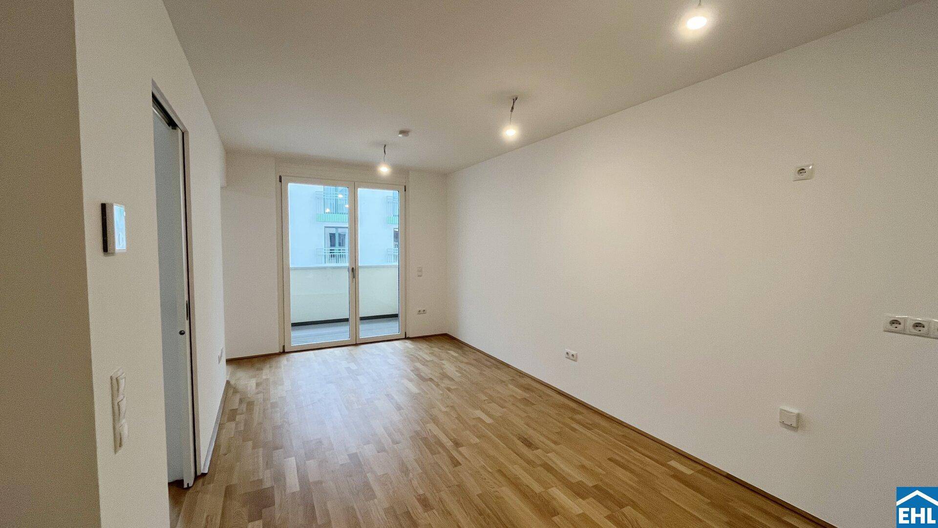 Geräumiger, unmöblierter Wohnbereich mit Holzboden und großen Fenstern zum Balkon.
