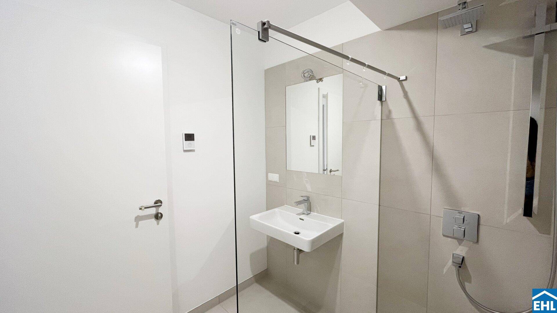 Helles Badezimmer mit moderner Duschkabine, Waschbecken und Spiegelschrank.