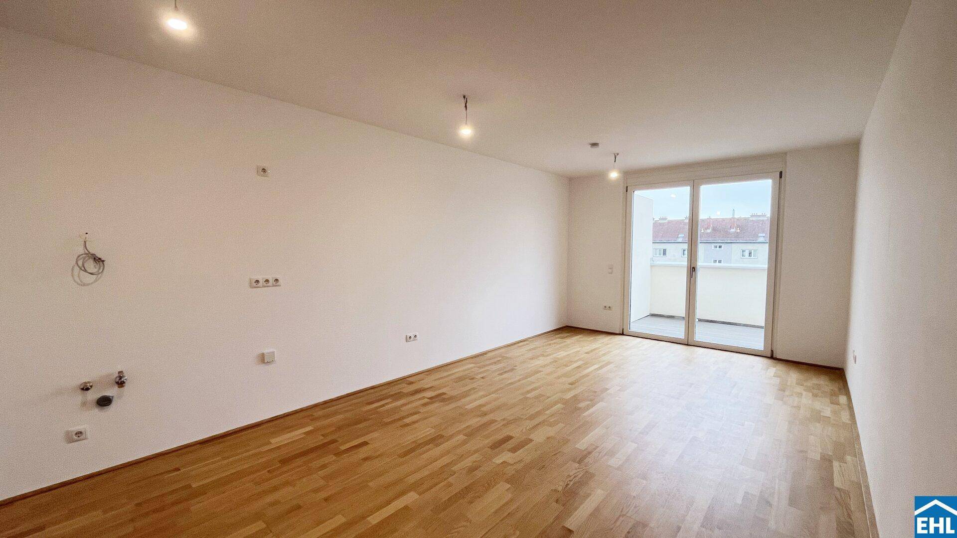 Geräumiges, leeres Zimmer mit Parkettboden und Zugang zu einem Balkon.