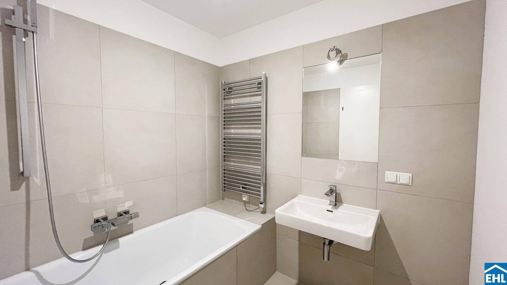 Modernes Badezimmer mit Badewanne, Dusche, beheiztem Handtuchhalter und hellen Fliesen.