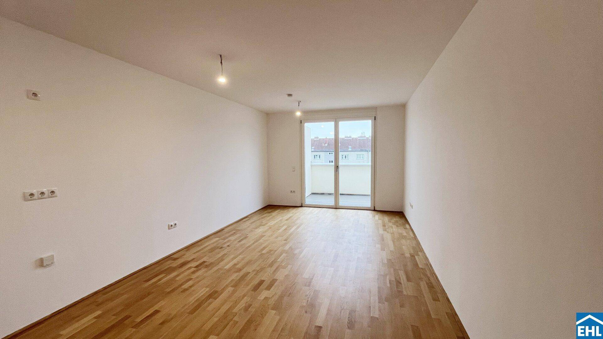 Helles, unmöbliertes Zimmer mit Holzboden und großen Fenstern zum Balkon.