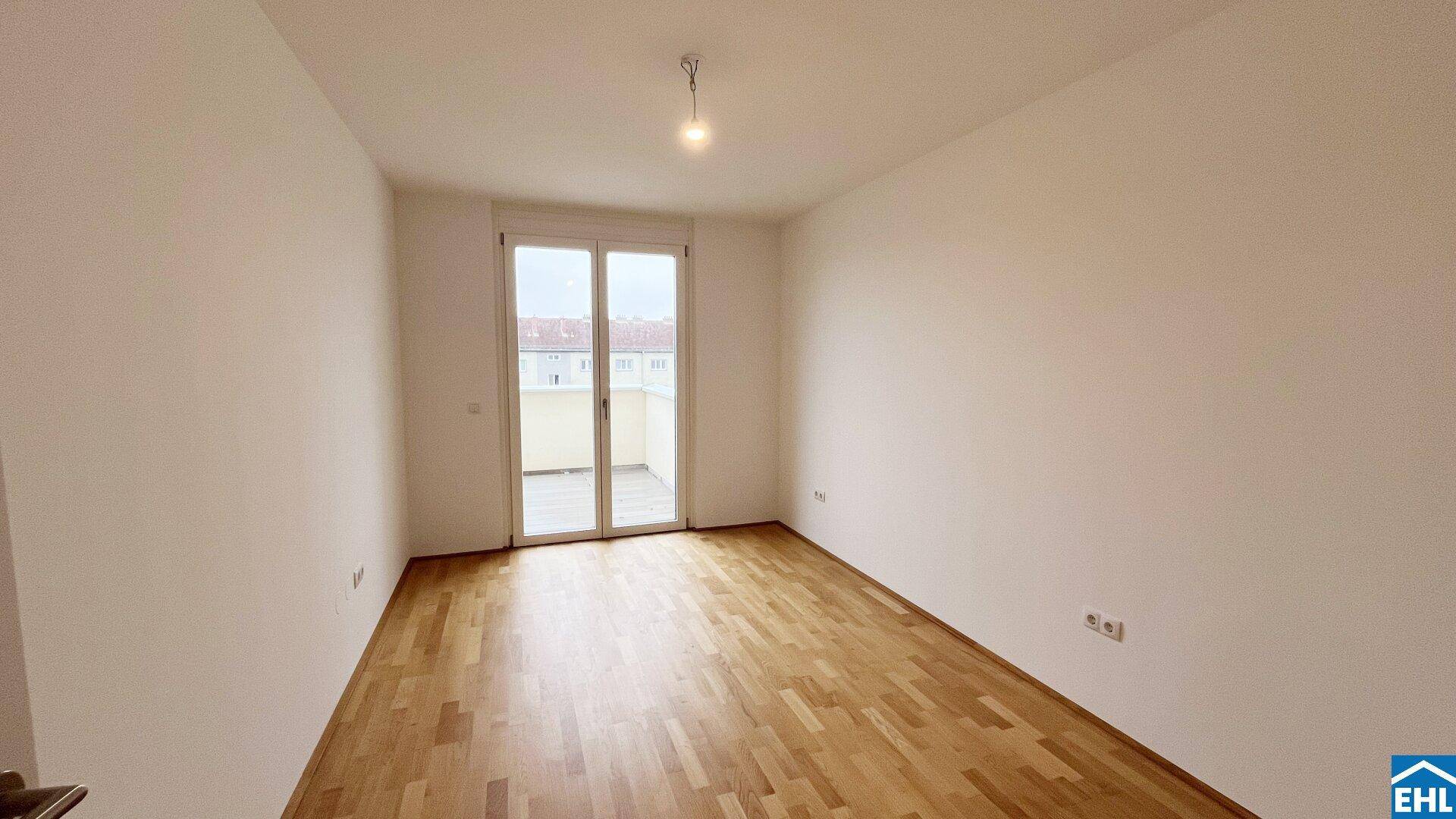 Helles, leeres Zimmer mit Holzboden und großen Fenstern, ideal als Schlafzimmer.