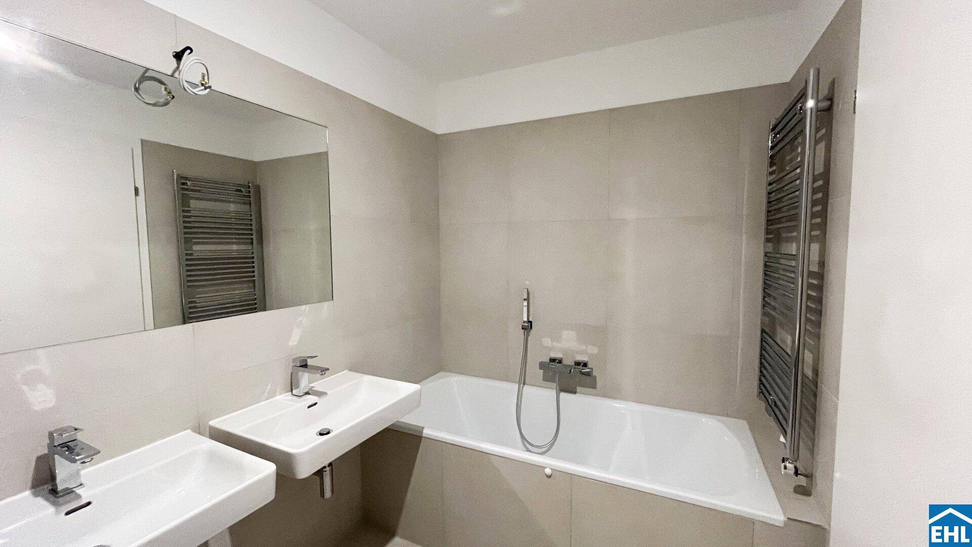 Helles Badezimmer mit Badewanne, Doppelwaschbecken und großem Spiegel, ausgestattet mit modernen Armaturen.