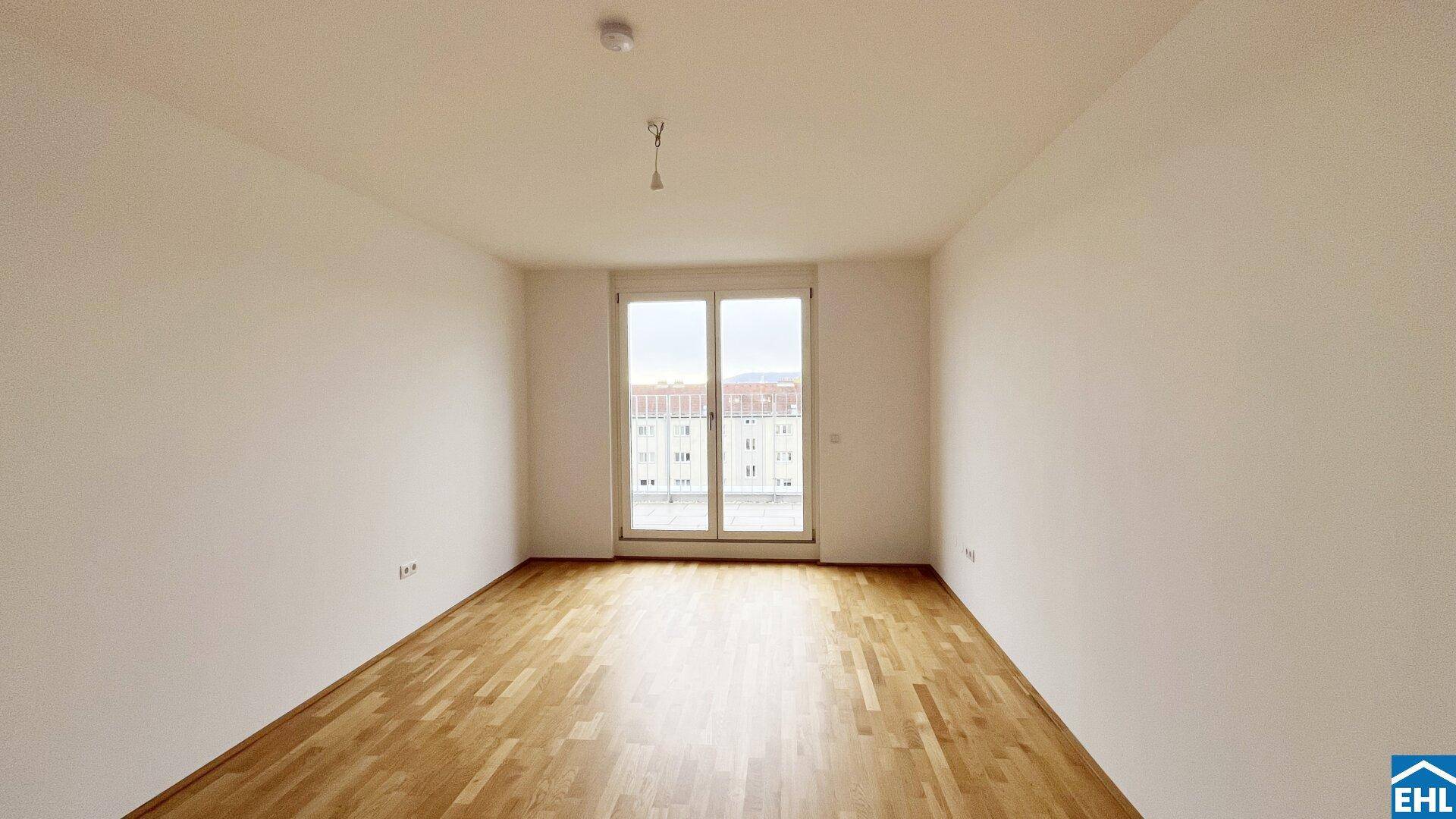 Leeres Wohnzimmer mit hellem Holzboden und großer Balkontür, bereit zur individuellen Gestaltung.