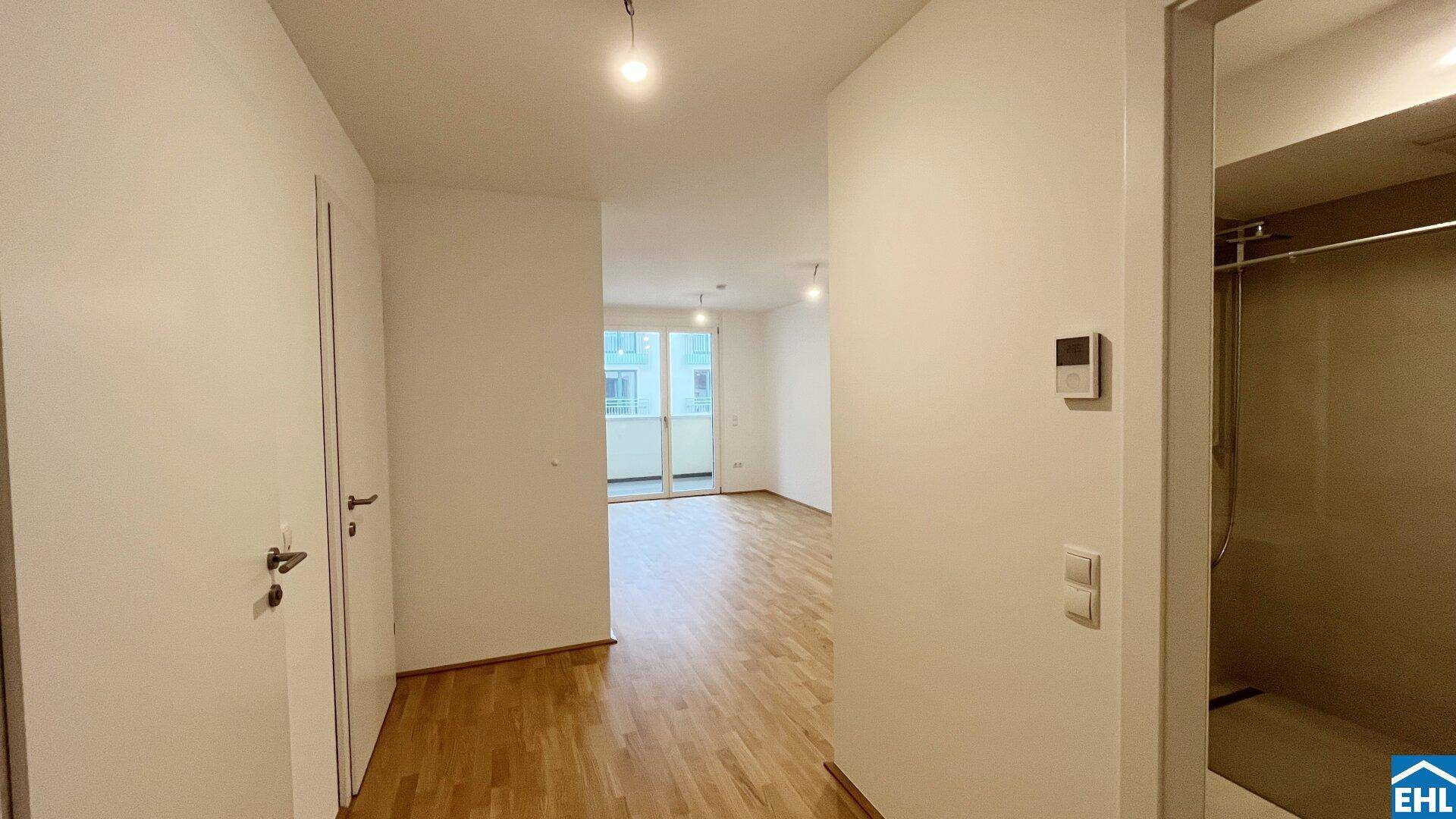 Heller Flur mit Holzboden, der zu verschiedenen Räumen führt, inklusive eines Badezimmers.