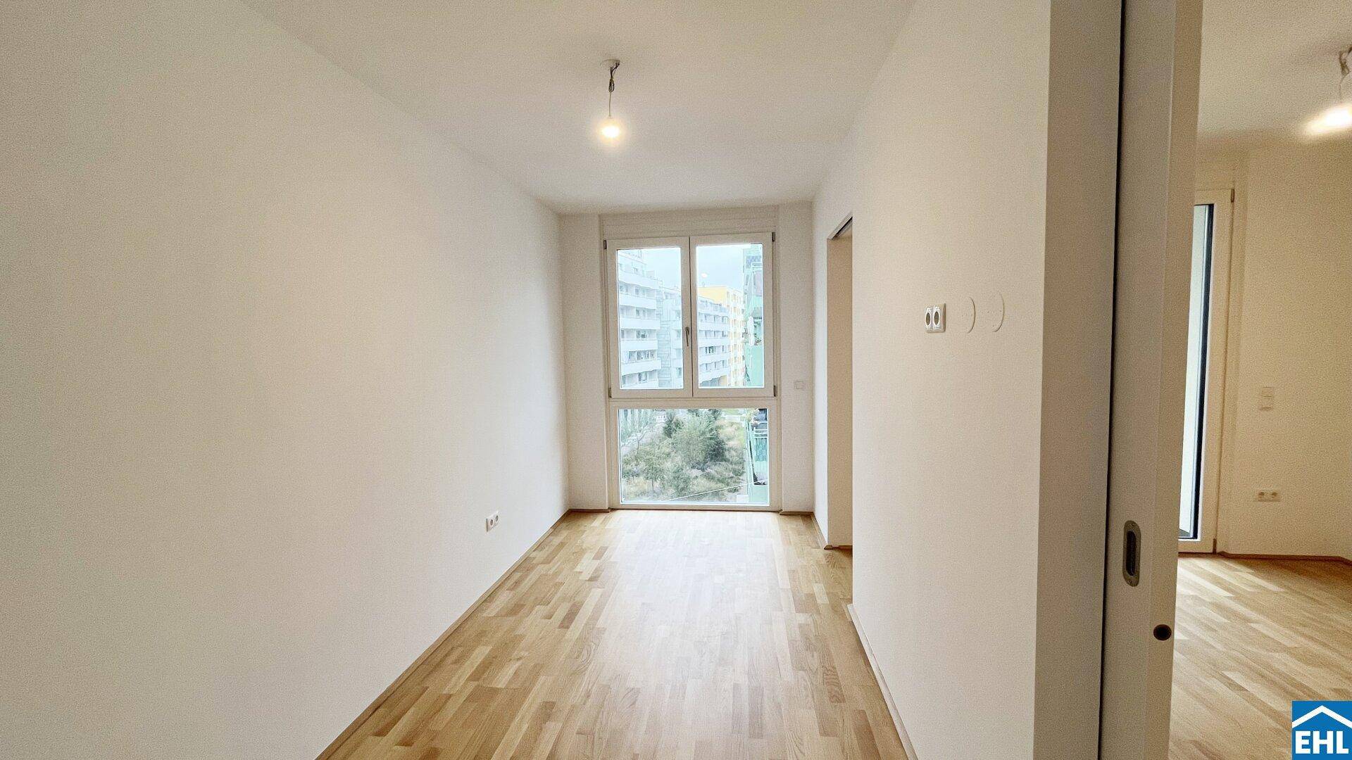 Unmöblierter Raum mit Holzboden und einem großen Fenster, das einen Blick auf die Stadt bietet.