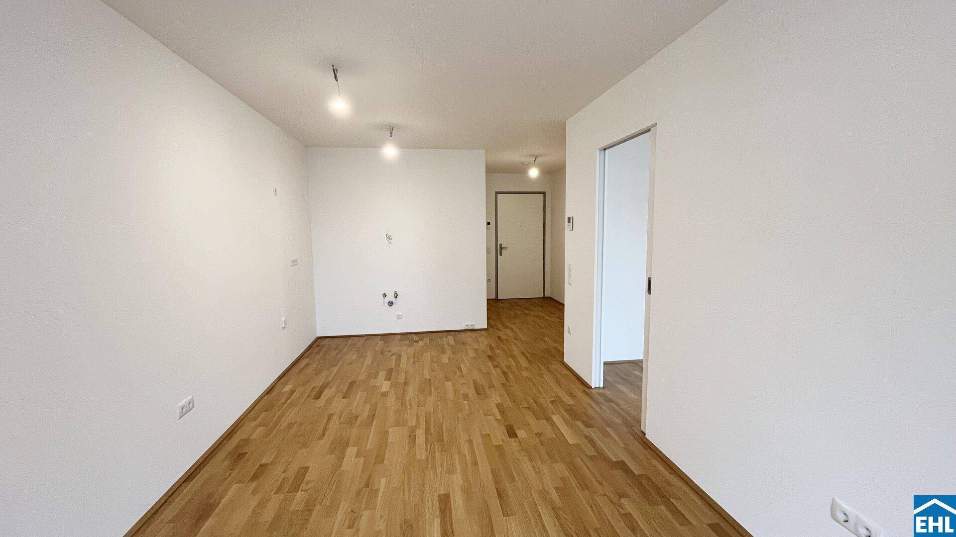 Leerer Raum mit Holzboden und weißen Wänden, vorbereitet für die Installation einer Küche.