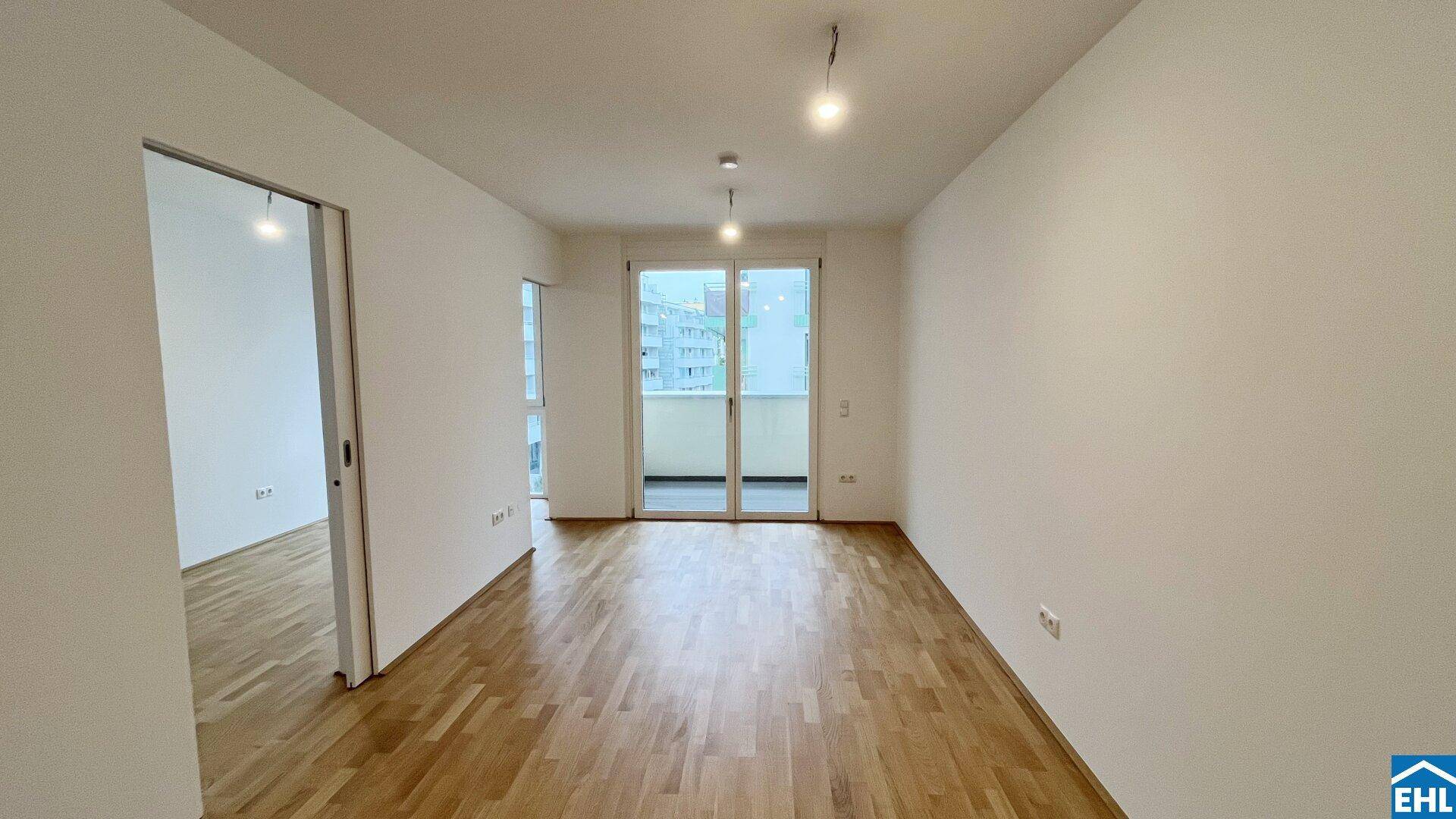 Heller, unmöblierter Raum mit Parkettboden und großen Fenstern, die zum Balkon führen.