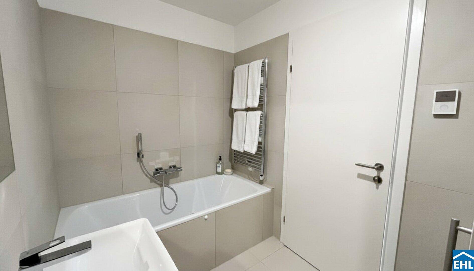 Modernes Badezimmer mit Badewanne, beheiztem Handtuchhalter und hellen, großformatigen Fliesen.