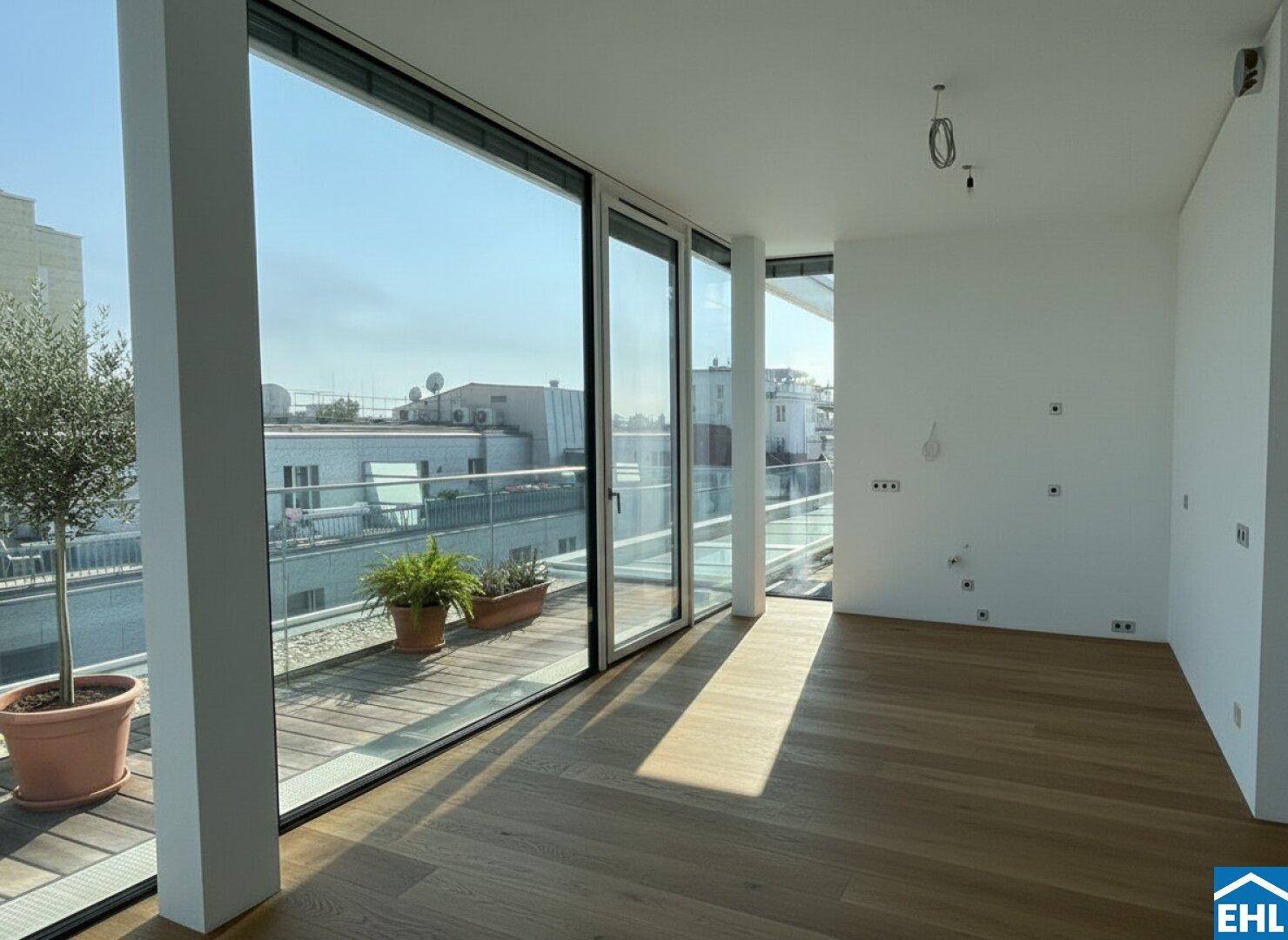 Heller, leerer Raum mit Holzboden und großen Fenstern mit Terrassenzugang.