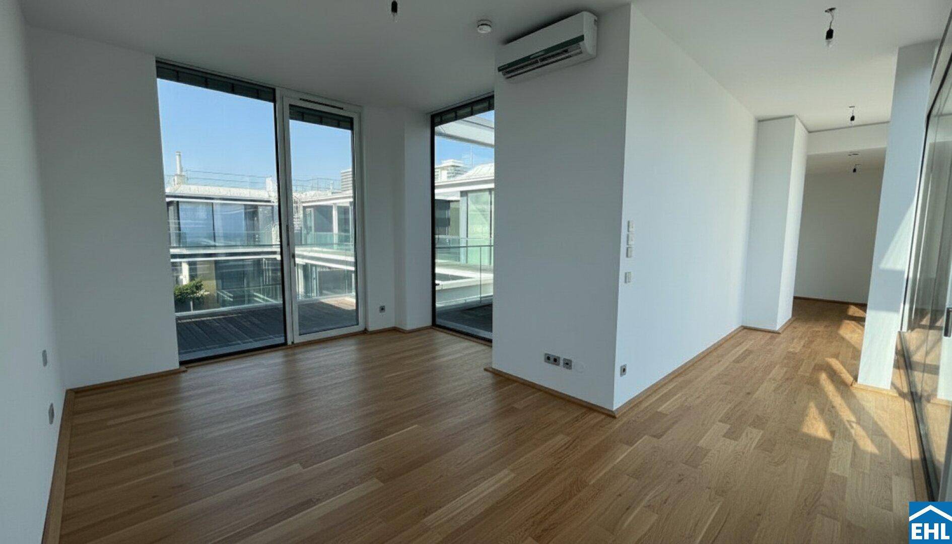 Leerer Raum mit Holzboden, großen Fenstern und viel Tageslicht.