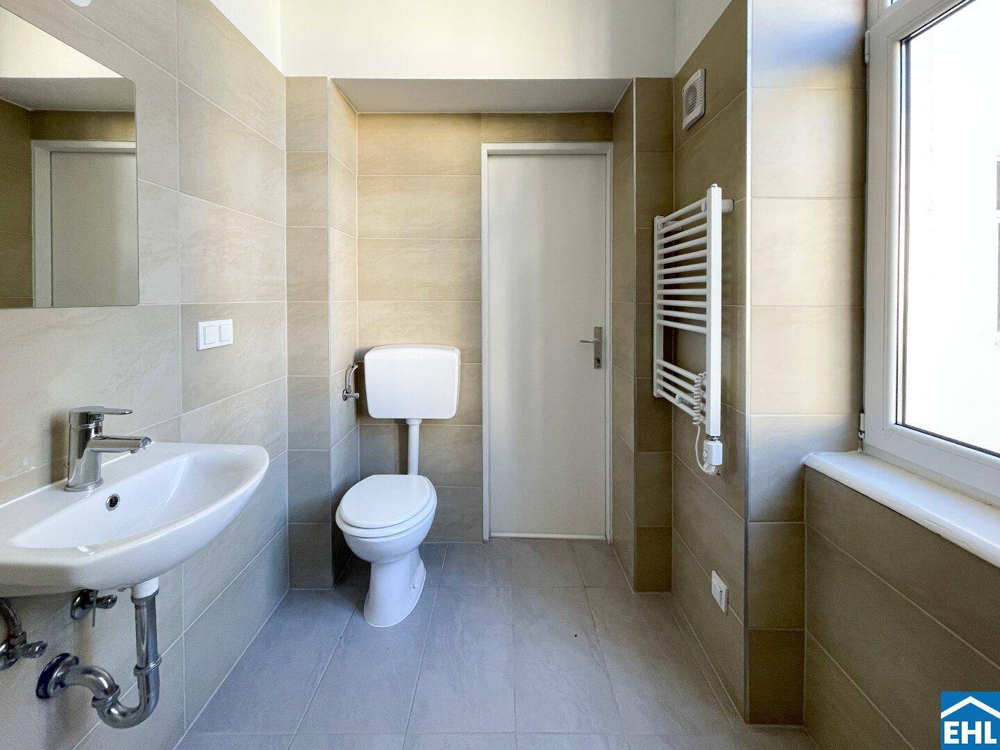 Modern gefliestes Badezimmer mit Waschbecken, Toilette und beheiztem Handtuchhalter.