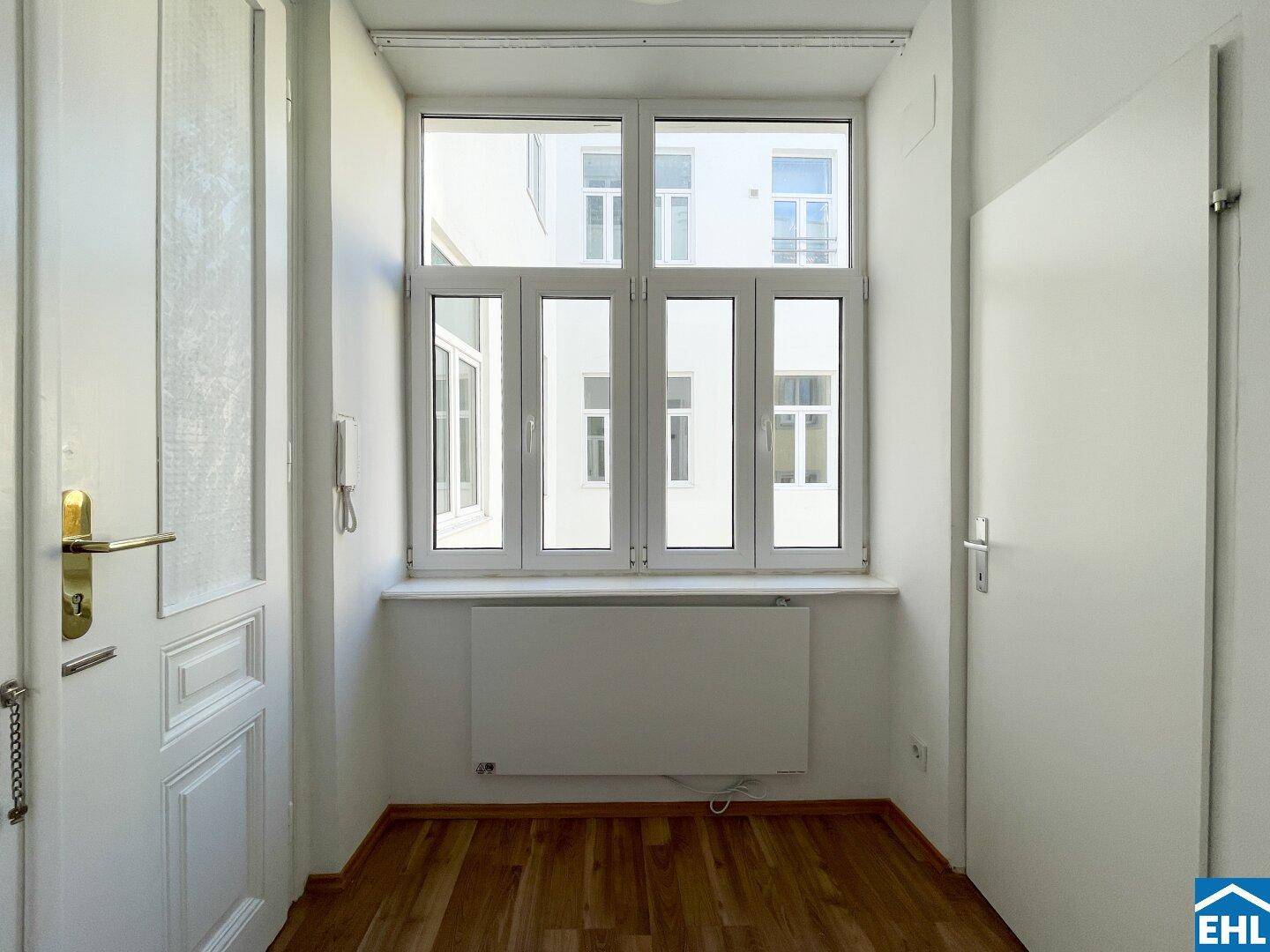 Eingangsbereich mit Holzboden und großem Fenster, das den Raum mit Tageslicht füllt.
