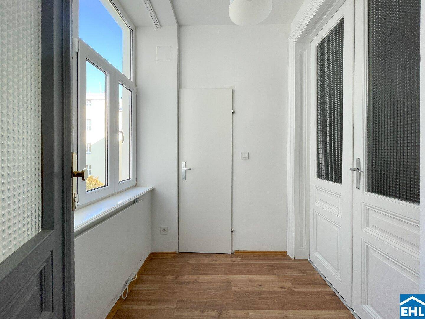 Heller Flur mit Holzboden und Fenstern, die viel Tageslicht in den Eingangsbereich bringen.