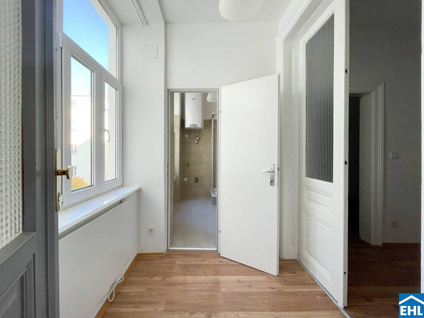 Flur mit Holzboden und Blick in ein helles Badezimmer, das durch eine offene Tür sichtbar ist.