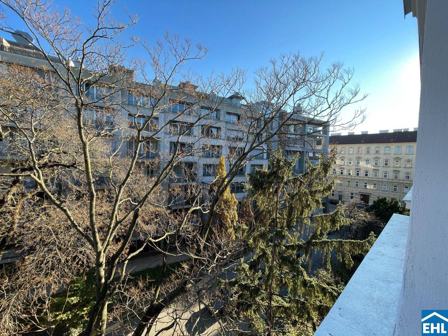 Ausblick von einem Balkon auf Bäume und die umliegende Stadtbebauung an einem sonnigen Tag.