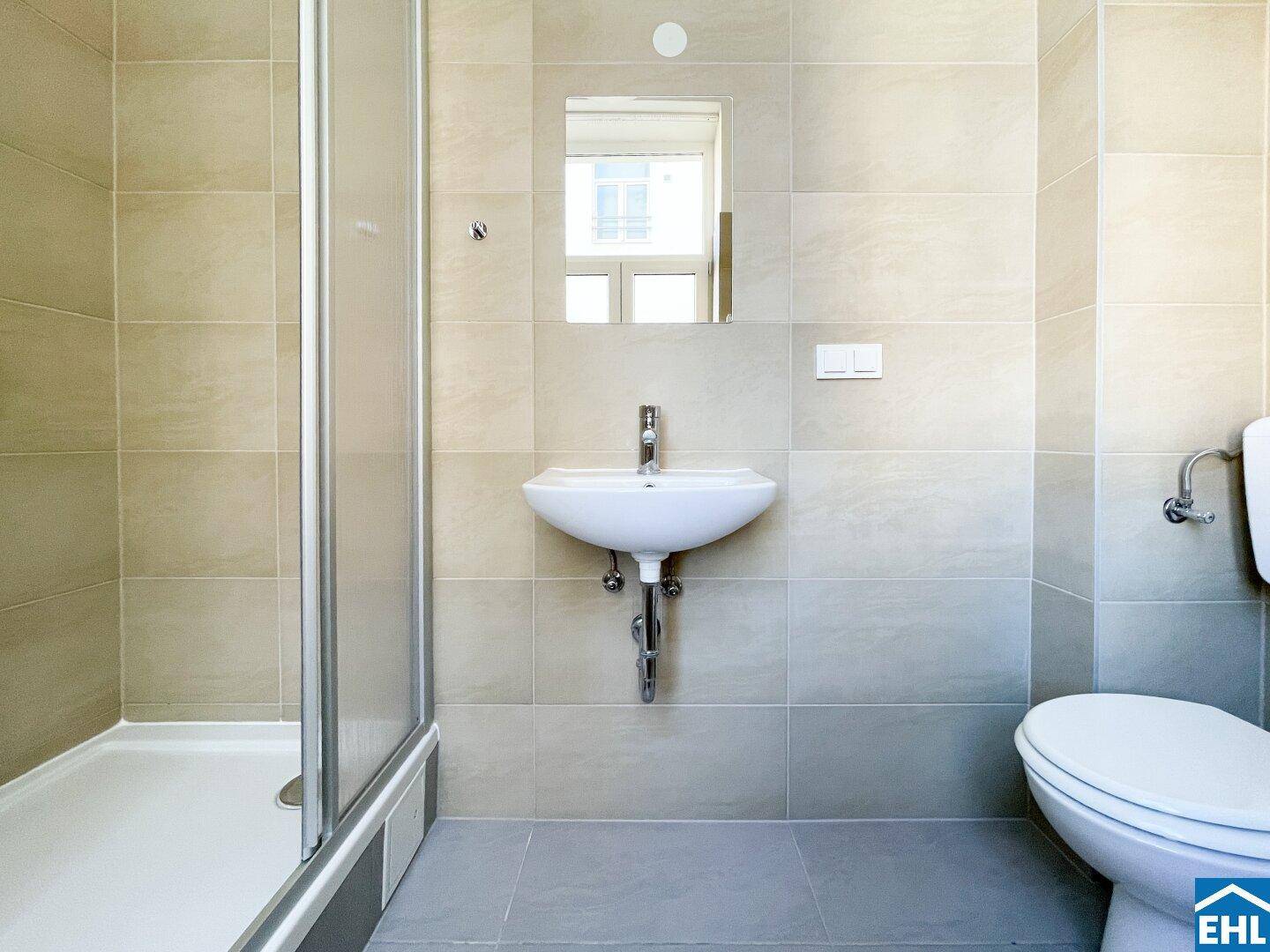 Modernes Badezimmer mit Duschkabine, Waschbecken und Toilette, hell gefliest.