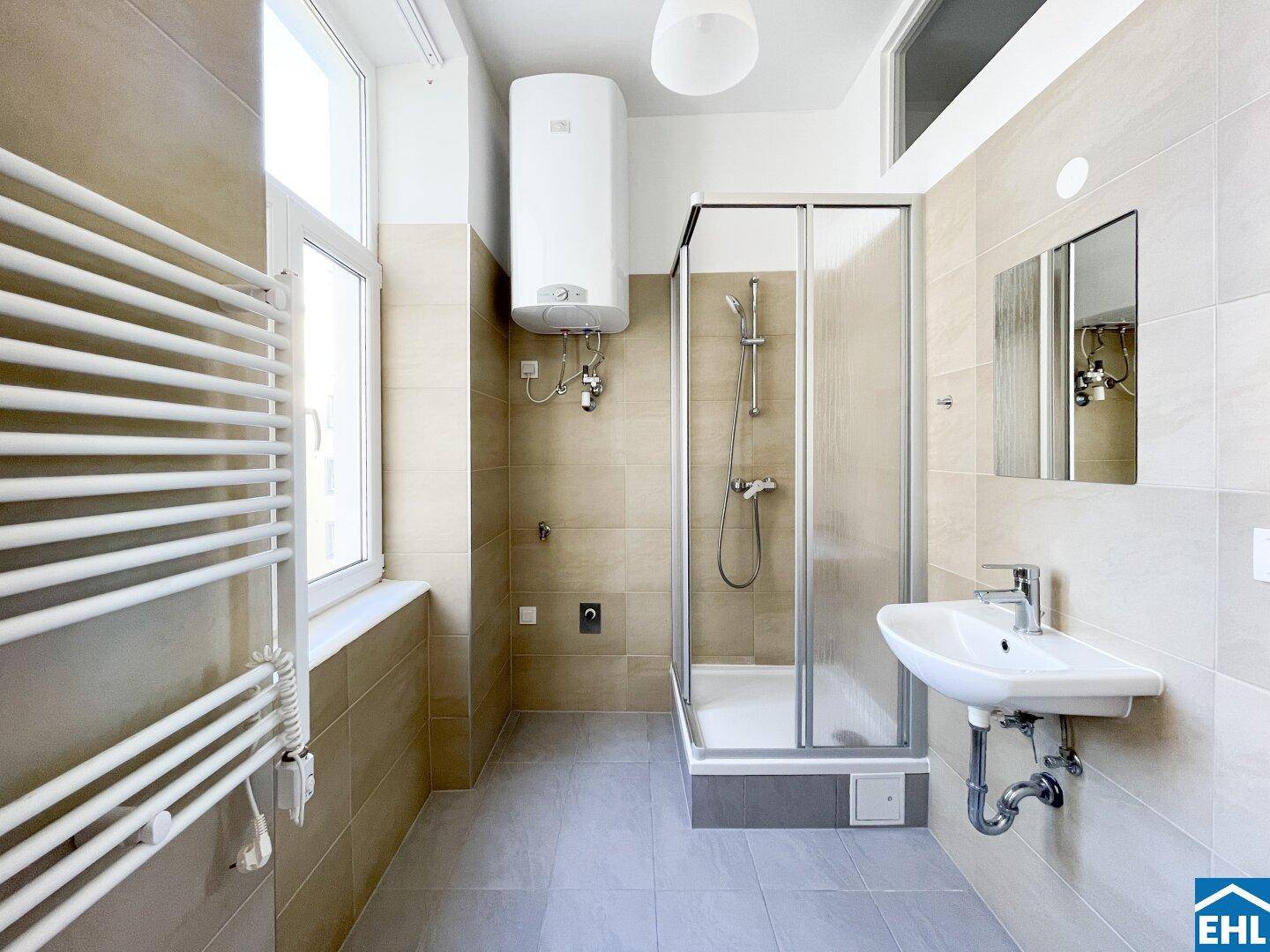 Helles Badezimmer mit Duschkabine, Waschbecken, beheiztem Handtuchhalter und Warmwasserboiler.