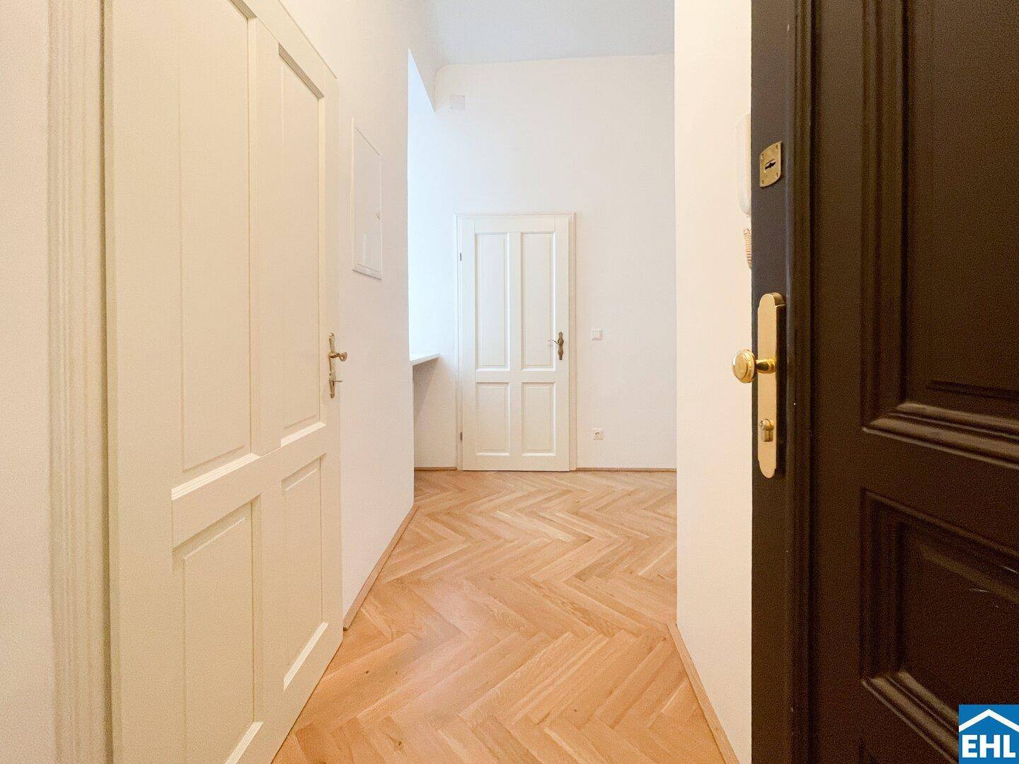 Eingangsbereich mit dunkler Eingangstür und hellem Fischgrätparkett, der in die Wohnung führt.