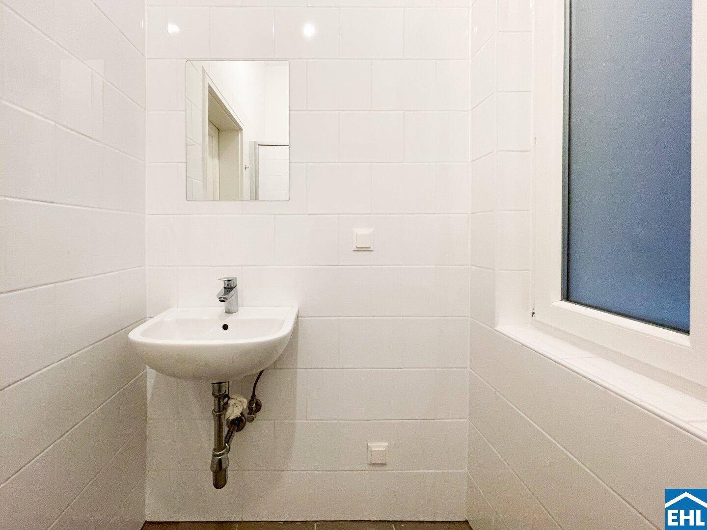 Modern gefliestes Badezimmer mit Waschbecken, Spiegel und Fenster für natürliche Belüftung.