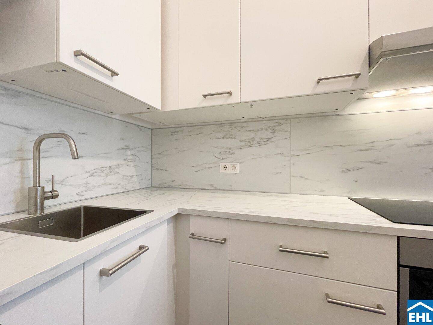 Detailansicht der modernen Küche mit weißer Arbeitsplatte, Spüle und eleganten Armaturen.