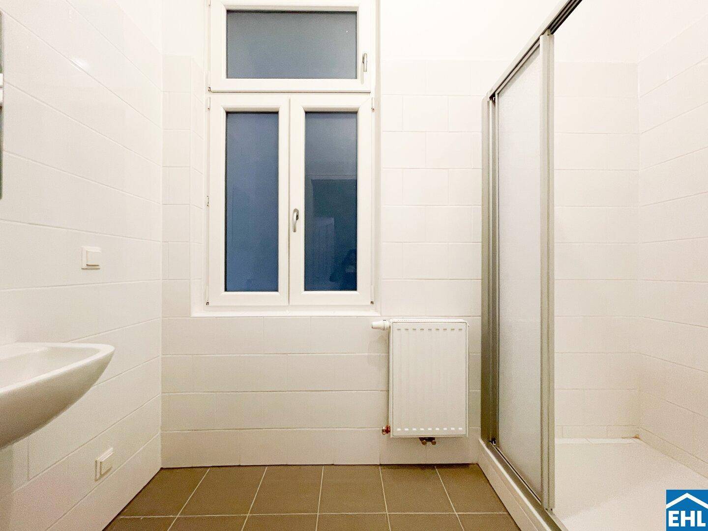 Helles Badezimmer mit Fenster, Heizkörper und Duschkabine, komplett gefliest.