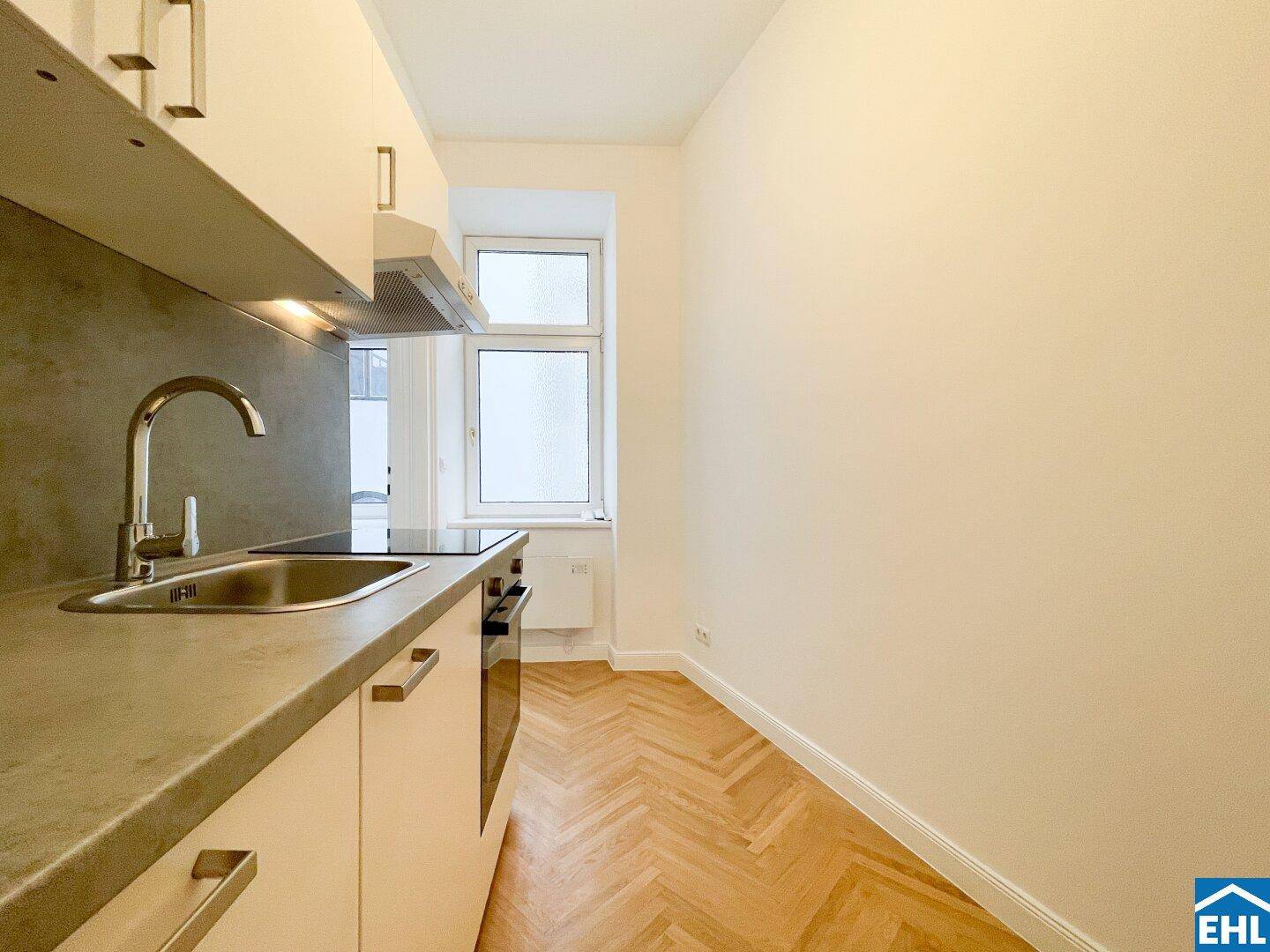 Kompakte Küche mit weißen Schränken, Spüle und Fenster für natürliches Licht.