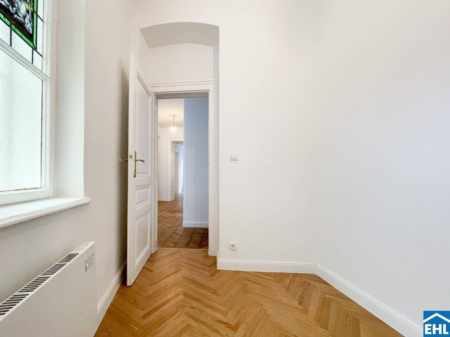 Kleineres Zimmer mit Fischgrätparkett und einem Fenster mit Buntglasdetails.