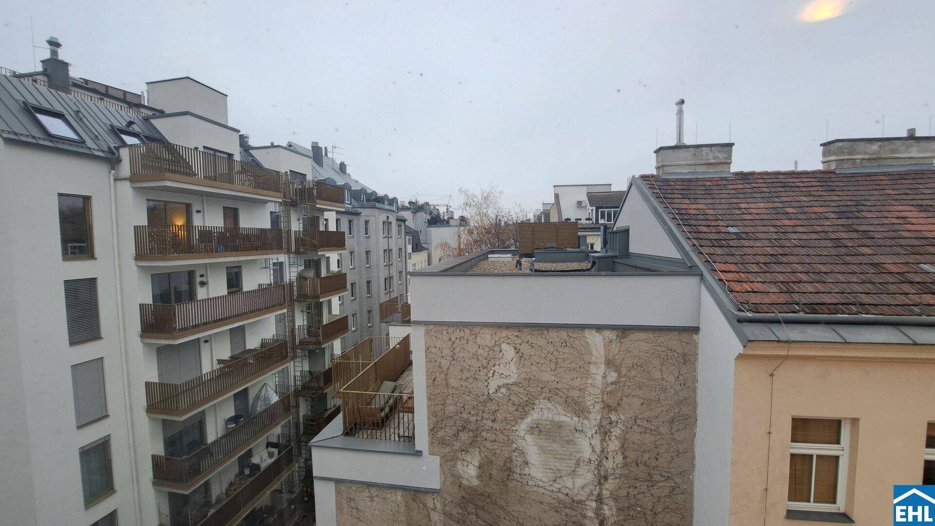 Blick aus dem Fenster auf umliegende Gebäude mit Balkonen und Dächern in urbaner Umgebung.