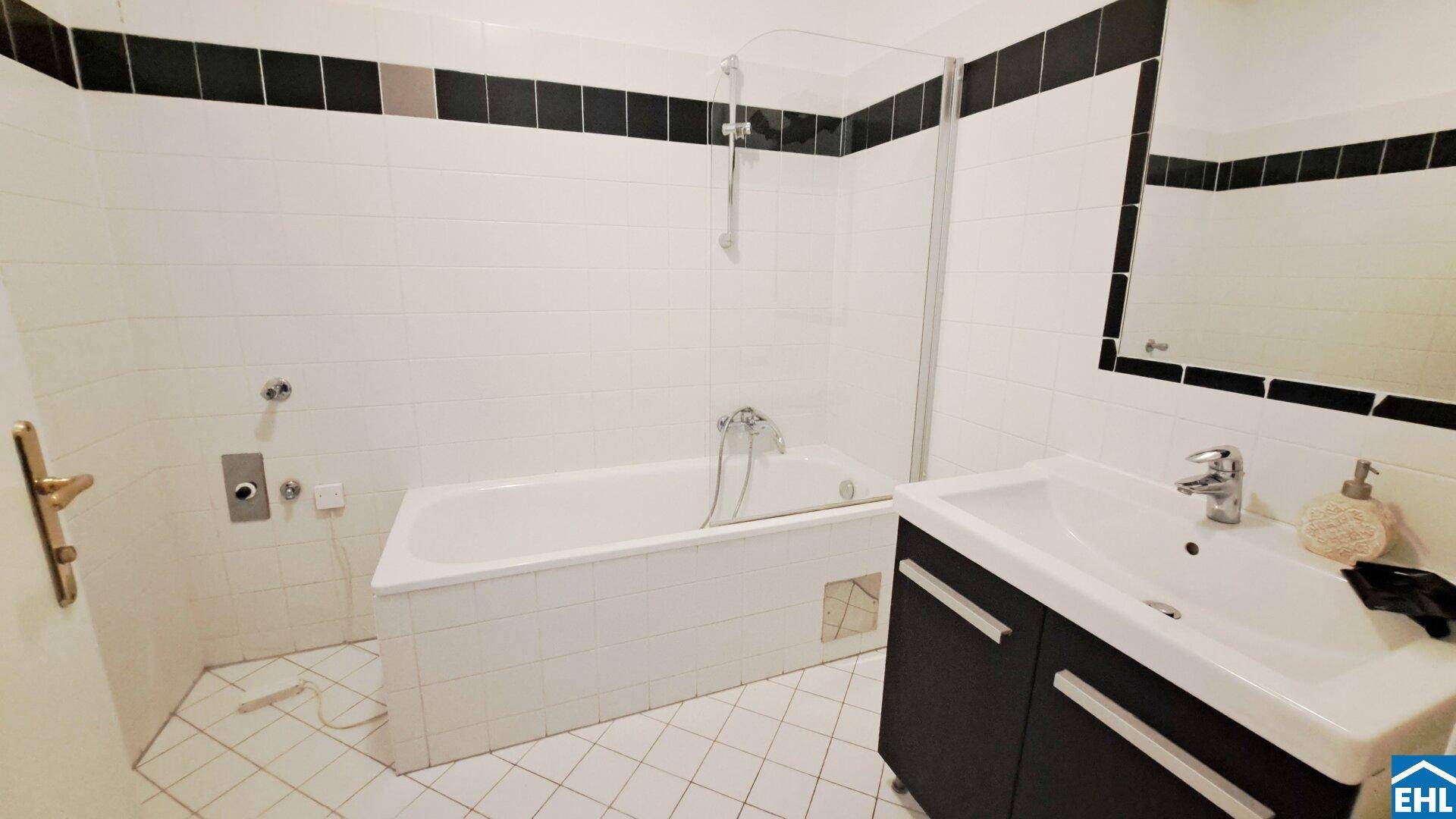 Modernes Badezimmer mit weißen Fliesen, schwarzem Akzent und Badewanne mit Duschabtrennung.